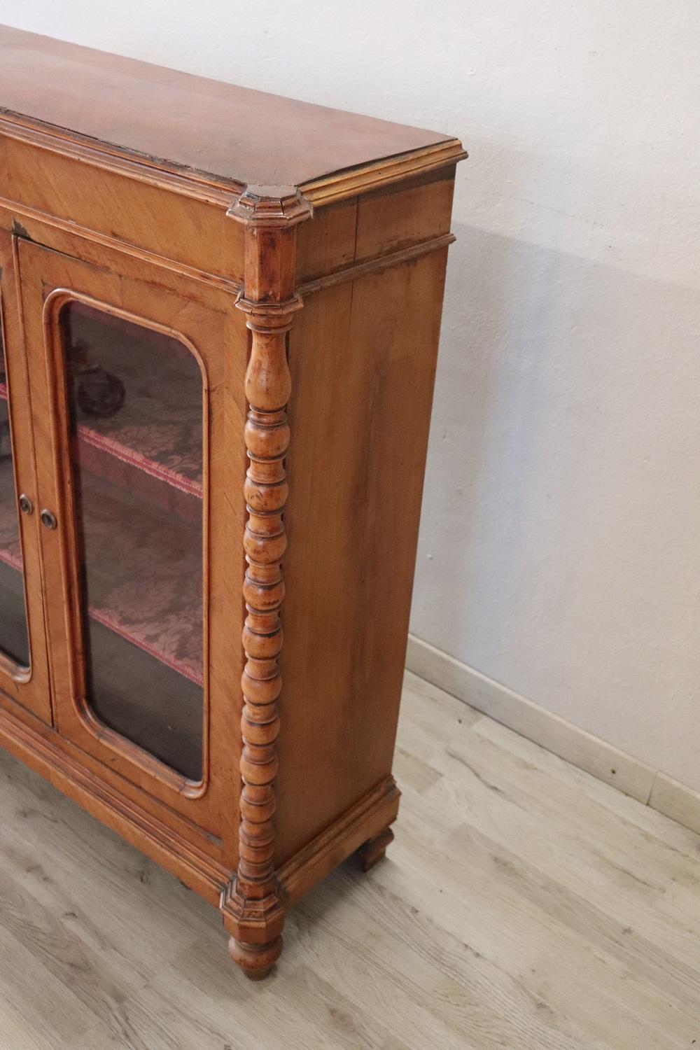 Elegant walnut antique Louis Philippe vitrine. Particular shape on the front with turned decoration on the sides. Interior lined in elegant red damask fabric and equipped with two shelves. Perfect for displaying your precious objects perfect