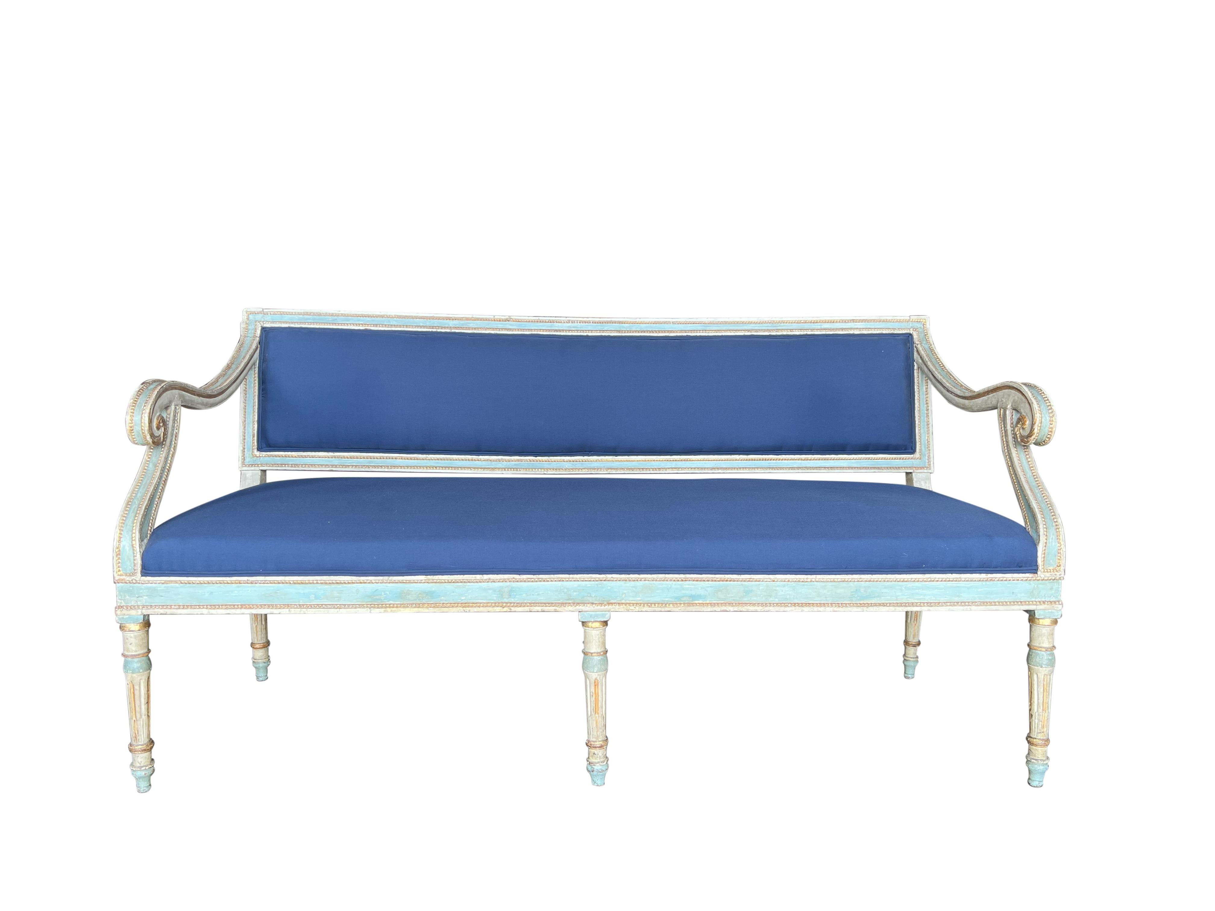 Italian Louis XVI style hall bench settee with sweeping arms, and 6 fluted legs. Antique beige and soft blue 2-tone patina highlighted by gold gilt details, Tuscany, circa 1820.  Professionally prepared for re-upholstery with restrung seat