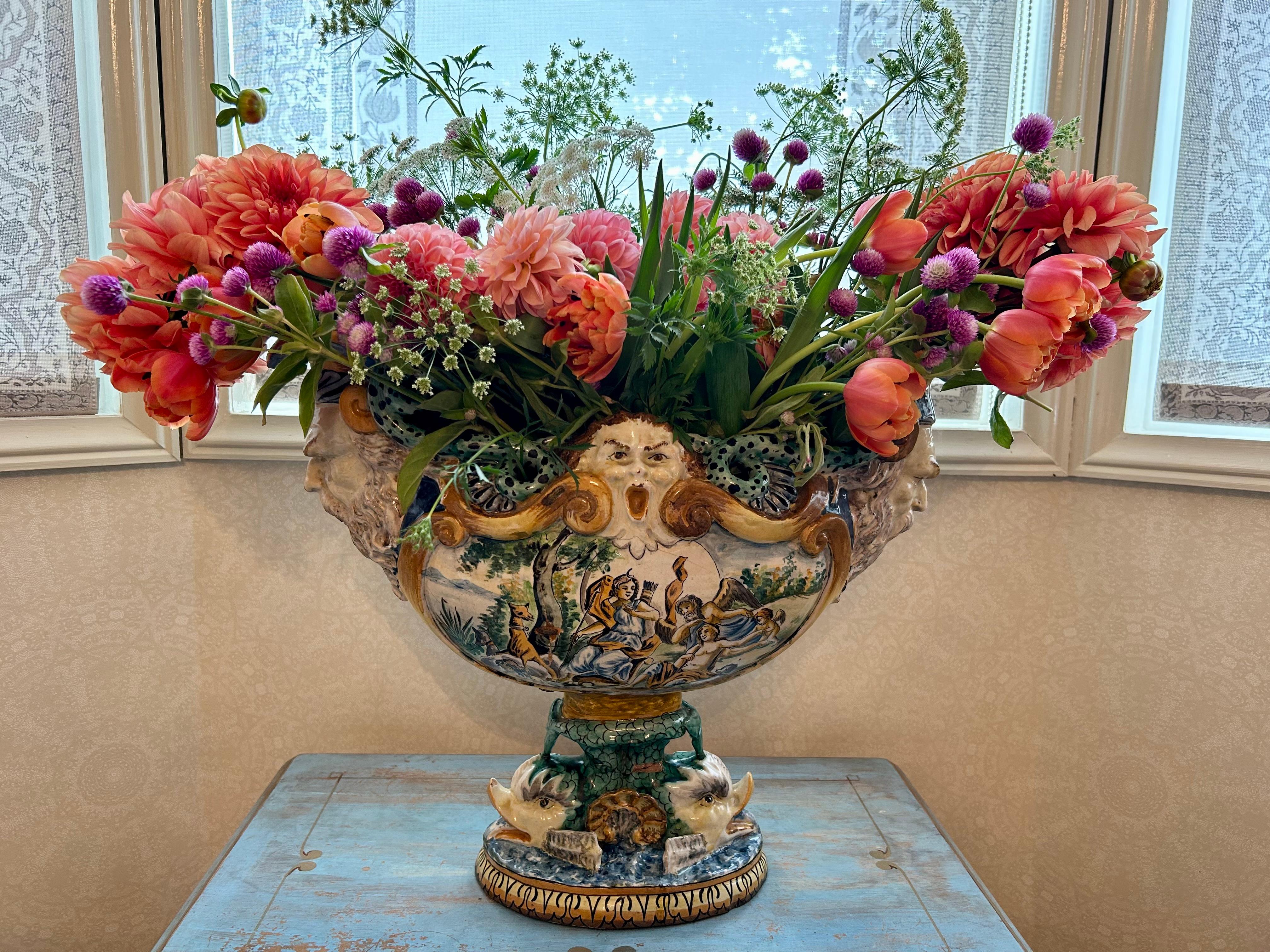 A fabulous figural boat shaped centrepiece/urn raised on a double dolphin base, with different painted mythological scenes throughout. The front and back of this urn are painted with individual scenes, and each end is shaped as the head of a god.