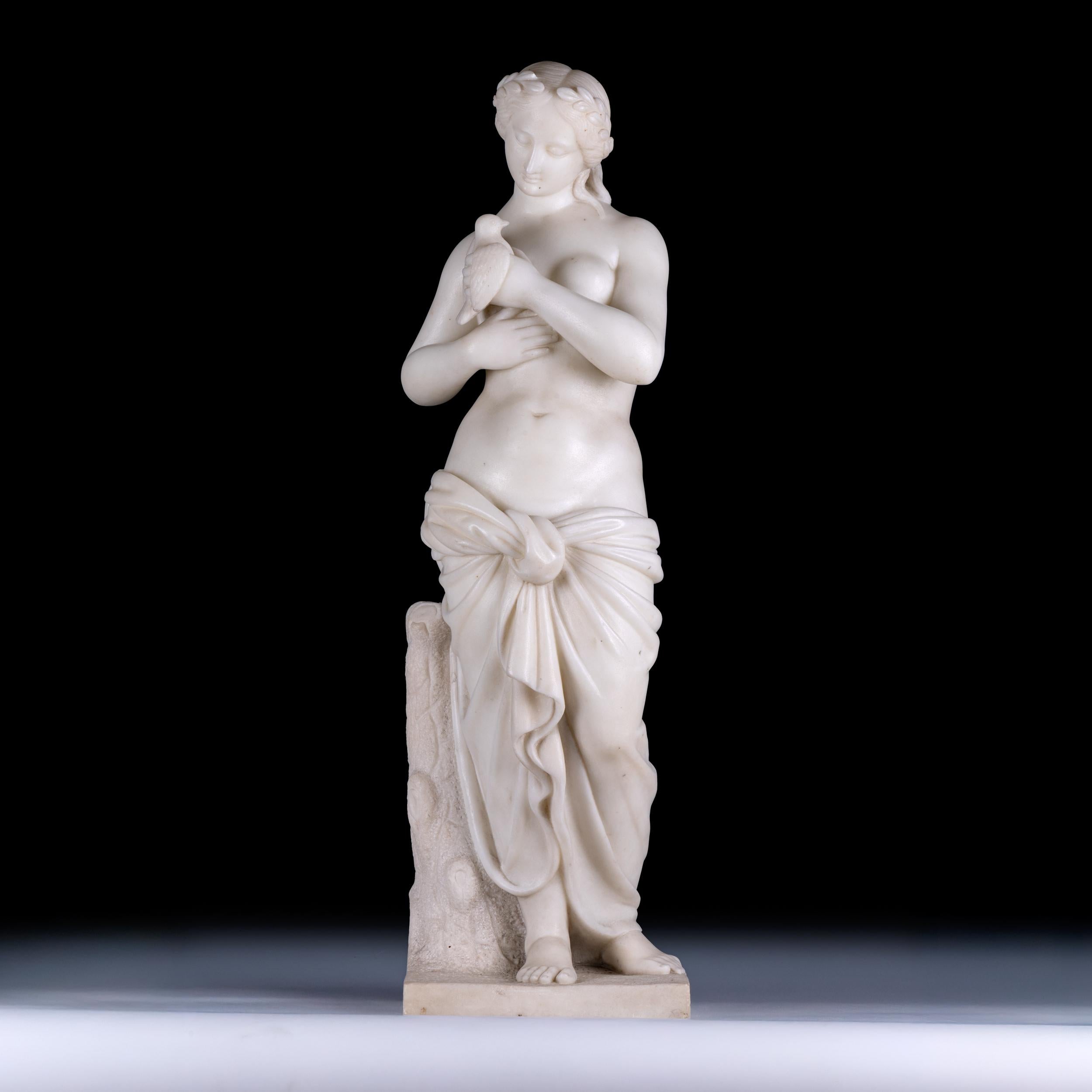 Magnifique figure en marbre d'un nu féminin classique tenant une colombe, avec une couronne de laurier dans les cheveux, représentant une femme debout portant une robe inférieure avec la poitrine exposée, appuyée contre une souche d'arbre,