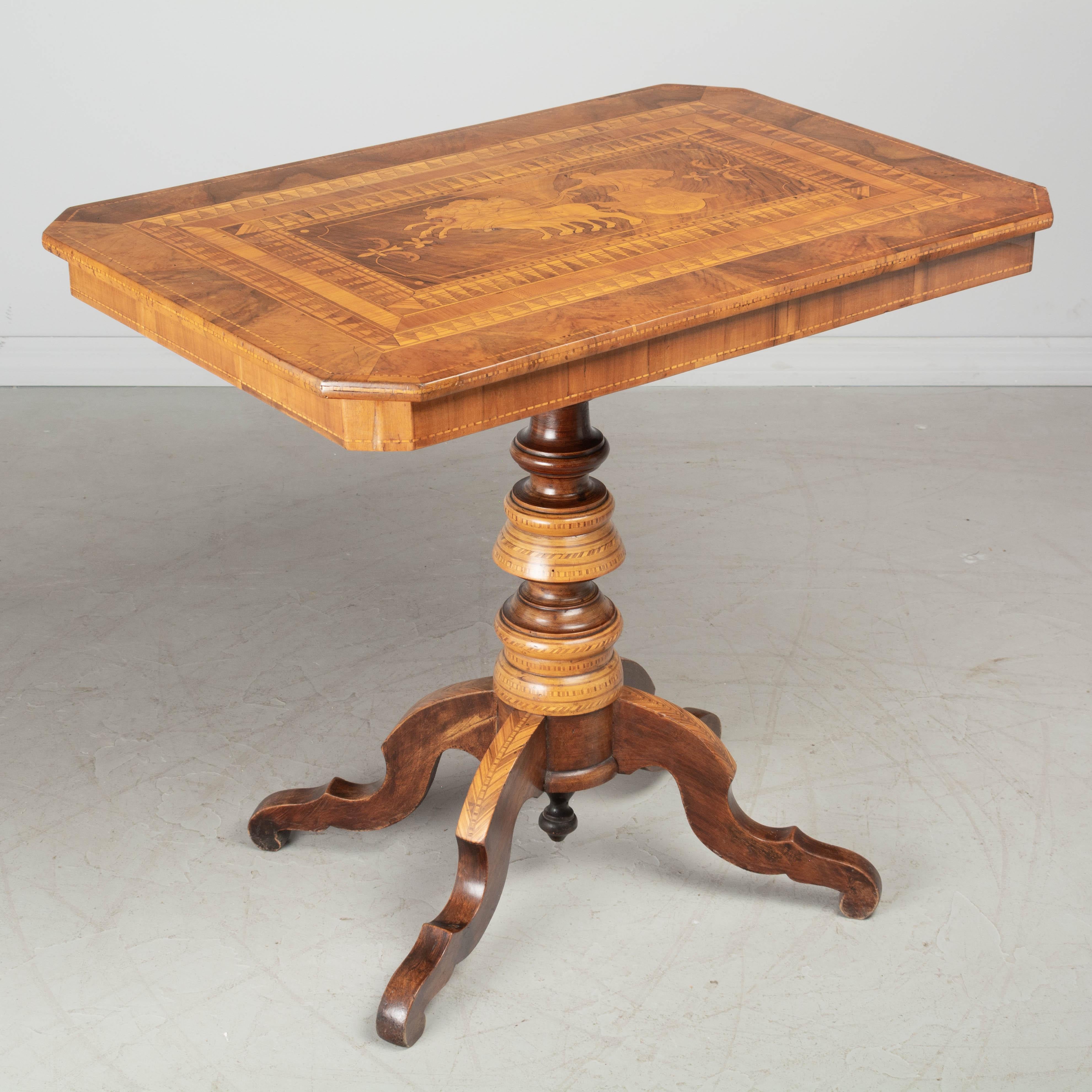 A 19th Century Italian marquetry tilt-top center table made of solid walnut with inlaid veneers of walnut and various woods. Marquetry top with Neoclassical imagery of The Sun Chariot surrounded by an elaborate decorative border. Sturdy turned