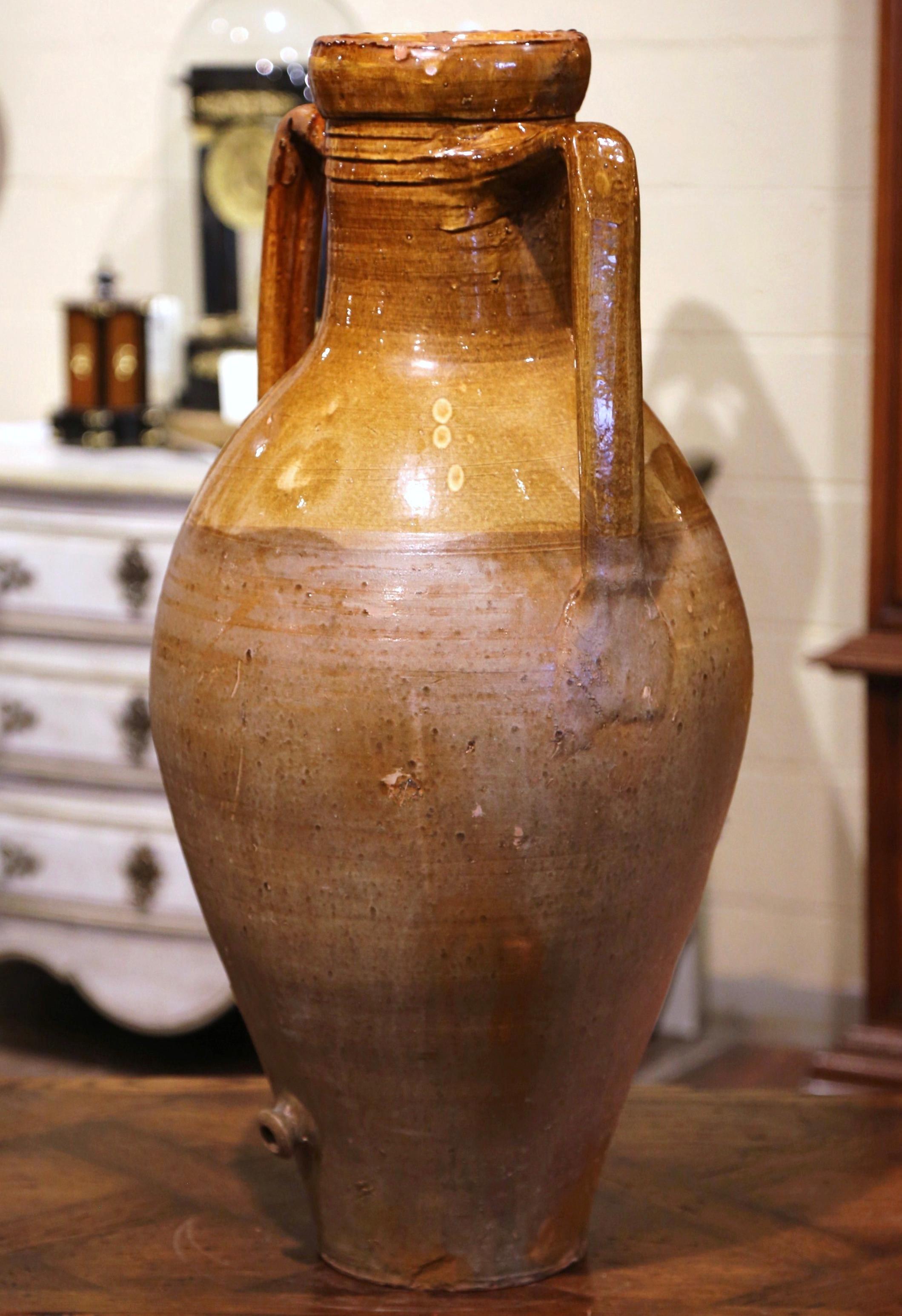 Add a Mediterranean touch to your indoor or outdoor spaces with this elegant antique Amphora. Crafted in Italy circa 1880, the earthenware vessel features double handles and lower spout at the bottom. The terracotta olive jar is in excellent