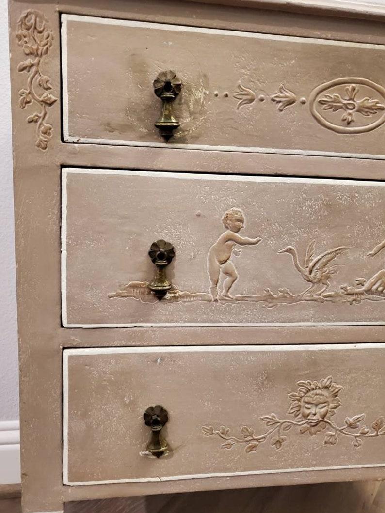 A Neoclassical style chest of drawers from the 19th century, acquired from the legendary American business magnate, T. Boone Pickens. Born in Italy, hand-crafted, carved and painted, decorated in relief renderings, the petite rectangular case fitted