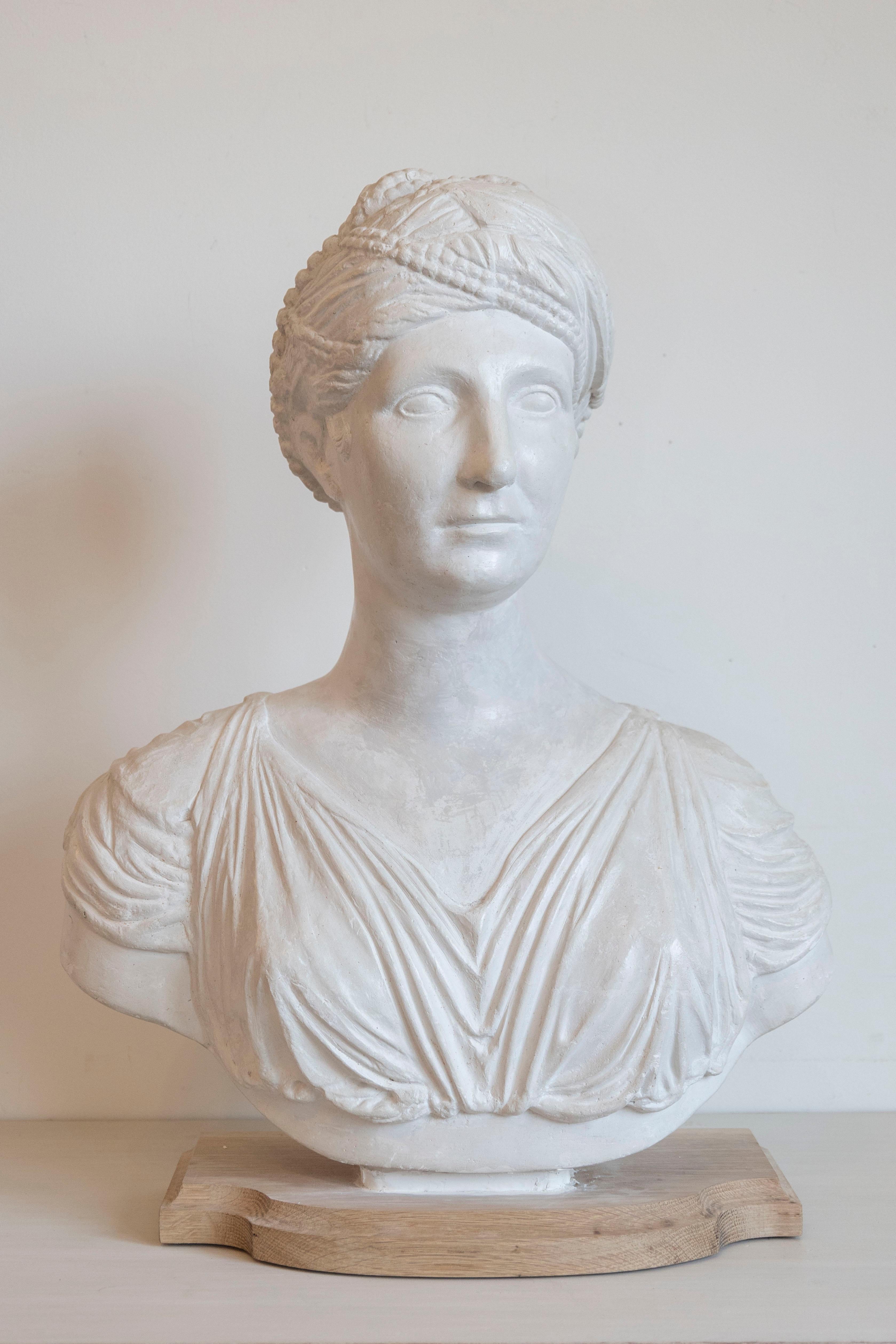 This elegant 19th-century Italian Neoclassical bust captures the timeless beauty and grace of a Roman woman, rendered in plaster with exquisite attention to detail. The subject’s serene expression, delicately sculpted facial features, and elaborate