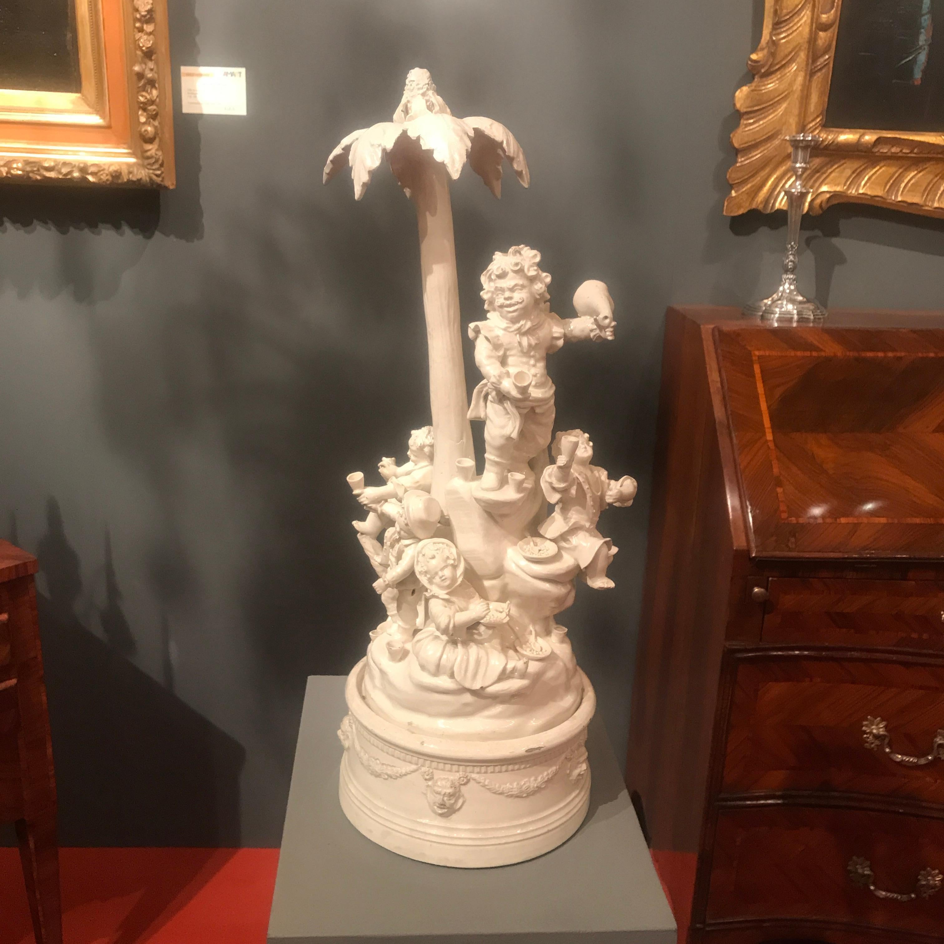 Un grazioso e molto decorativo centrotavola circolare figurativo in ceramica bianca italiana che raffigura un gruppo di nani intorno a una palma, in atteggiamento di festa e brindisi. Questa antica opera in ceramica italiana, risalente all'inizio