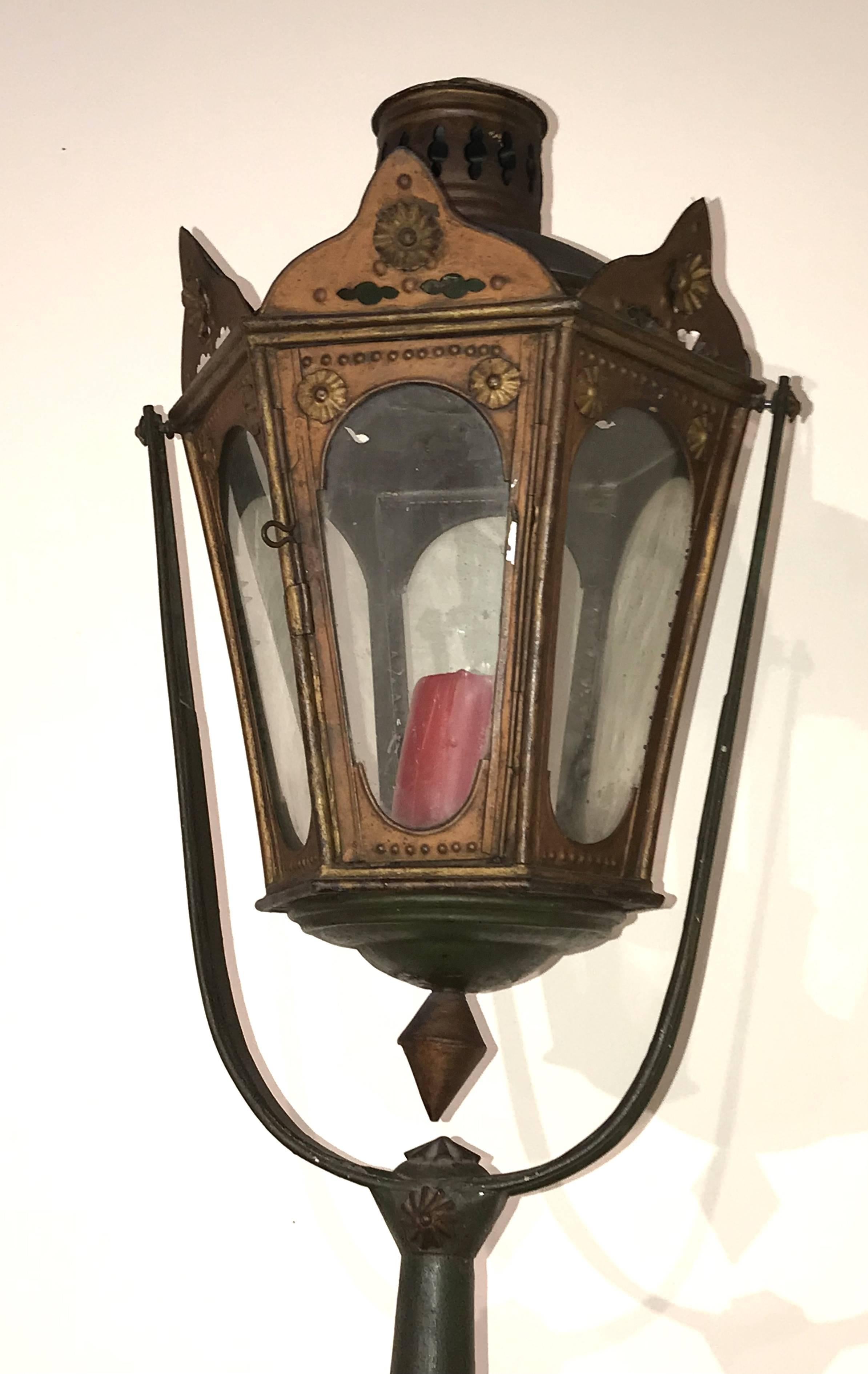 A fine example of an Italian / Venetian gondola lantern with painted hexagonal metal surround with rosette decorated crests, glass panels intact, suspended on a swinging metal support in old green paint, mounted on a red and white striped post,