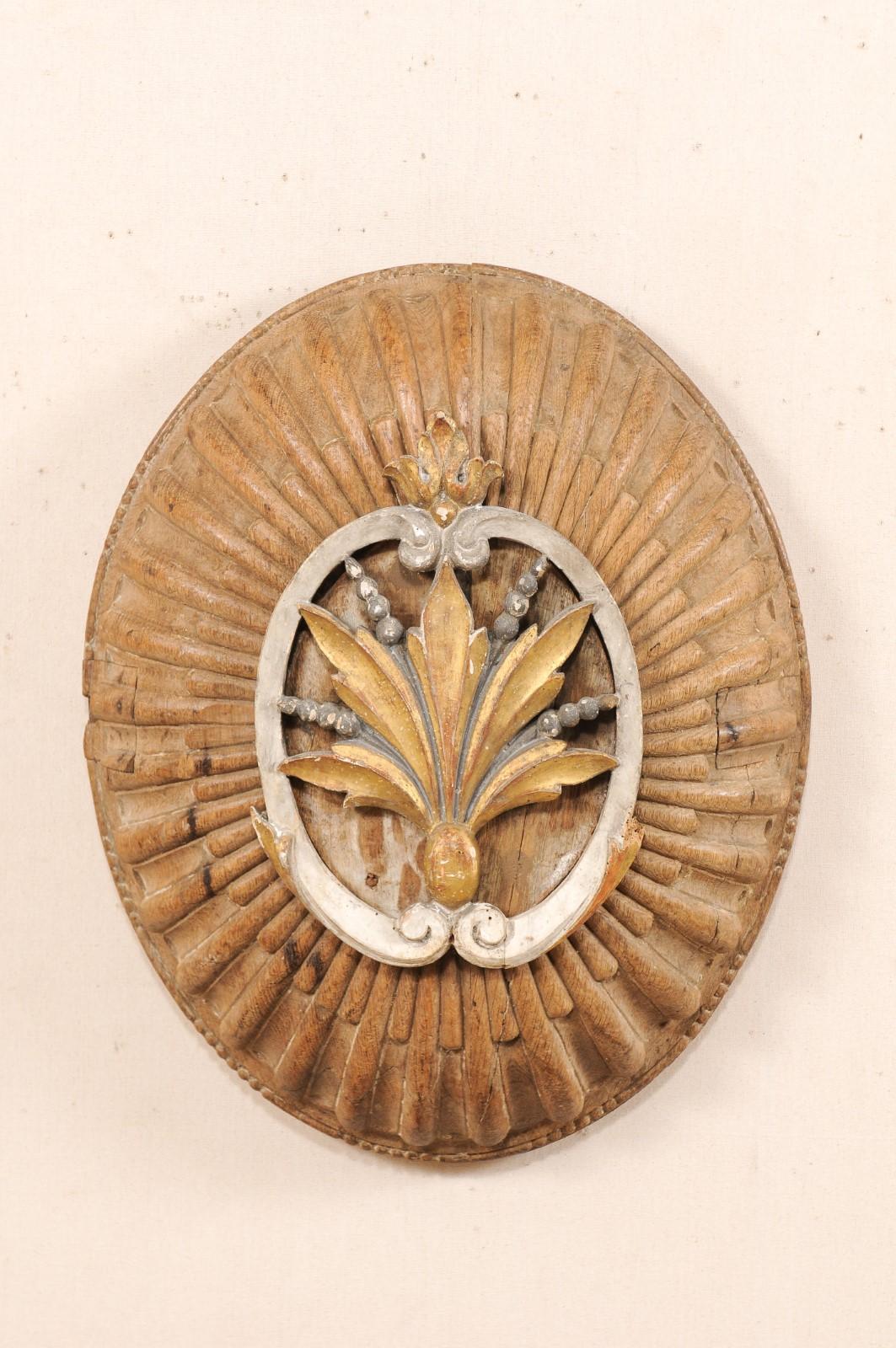 An Italian carved wood fragment wall ornament from the 19th century. This antique wall plaque from Italy has a domed, oval-shape, hand-carved with emphasis at raised center plaque with leaf motif framed within a pair of c-scrolls. Undulating rays