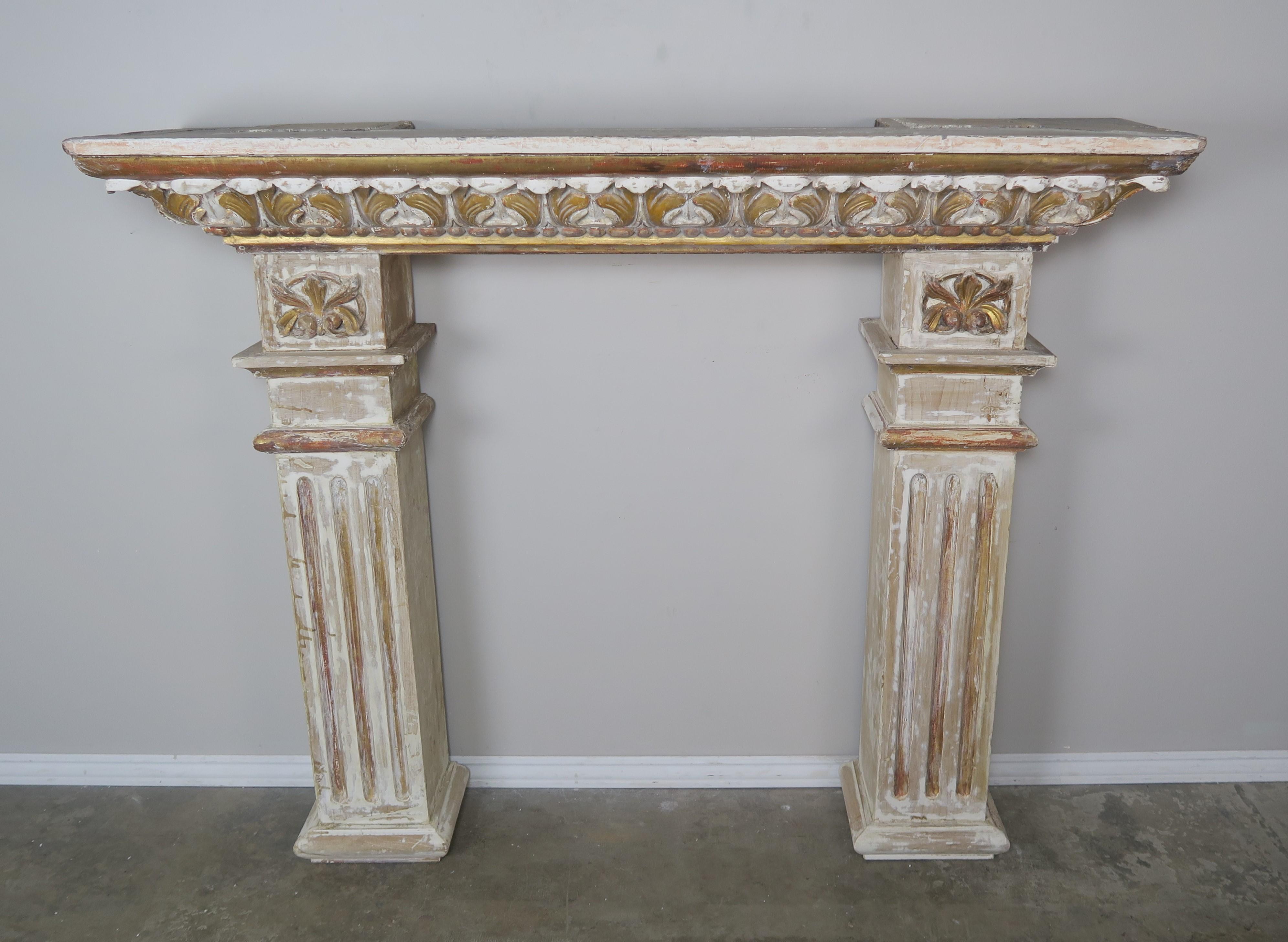 19th century Italian neoclassical style painted and parcel gilt carved wood fireplace mantel. Carved acanthus leaf detail across the top of the piece. Worn painted finish with highlights of gold leaf throughout.
 