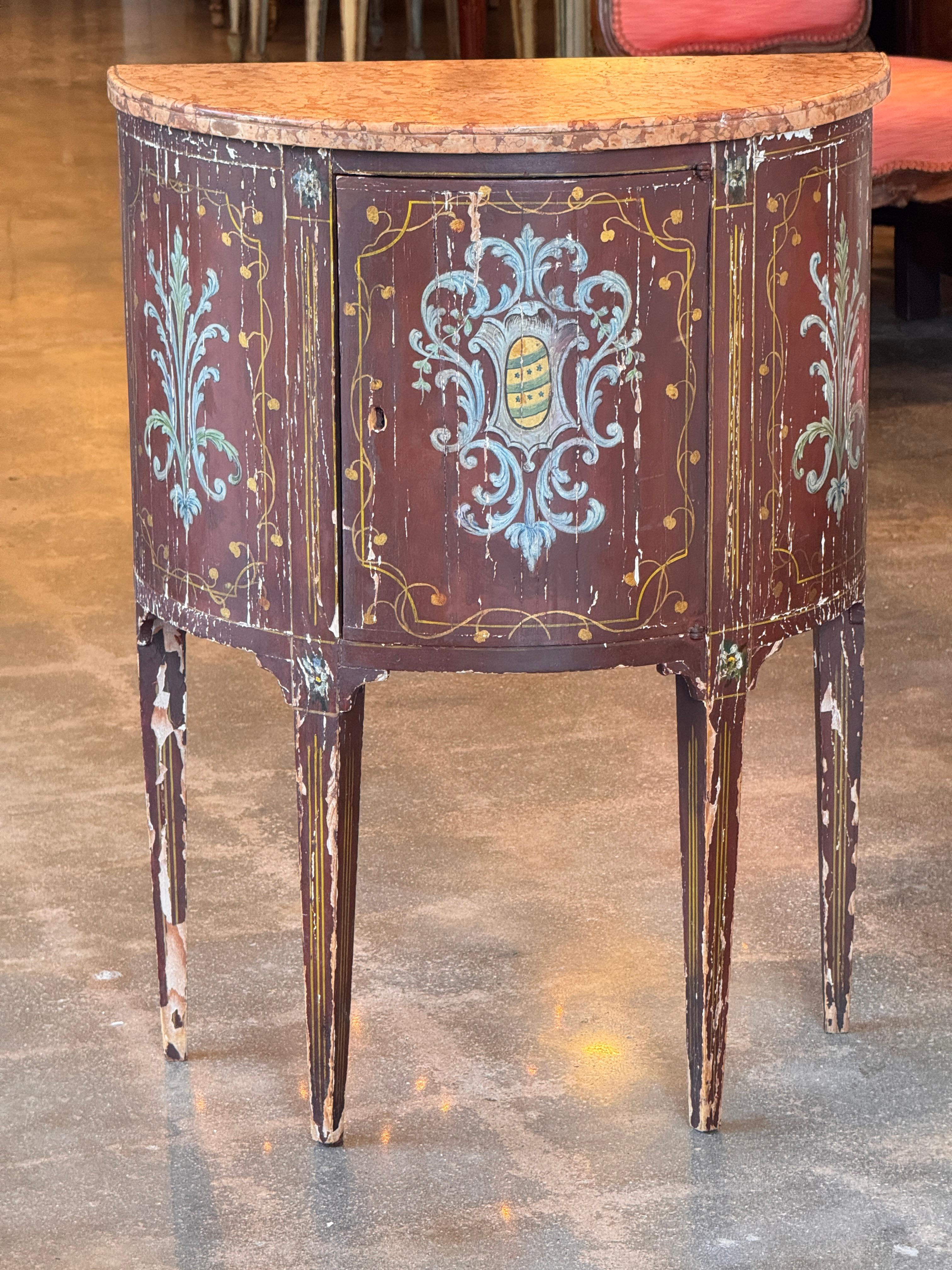 Cabinet italien peint du XIXe siècle, décoré de rinceaux stylisés et d'un écusson héraldique central, le tout en polychromie vieillie sur fond rouge. Le plateau en marbre et les pieds effilés complètent sa forme gracieuse. L'intérieur comporte deux