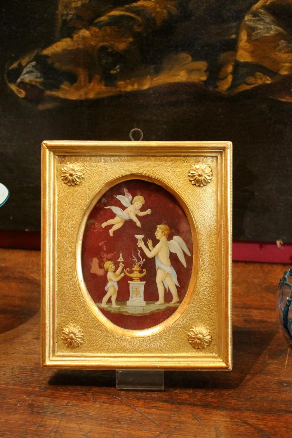 This lovely late 19th Century or turn of the century Italian oil painting on glass features a Neoclassical scene with putto.
The winged cherubs and the architectural elements are rendered in soft pastel tones while the background is red. Both the