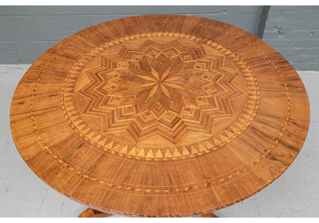 The round top with two outer bands and edge with checked string inlays. A large elaborate parquetry star shaped in the center with outer triangular inlaid band. Raised on a turned baluster support with checked inlays and a tripod base with inlaid