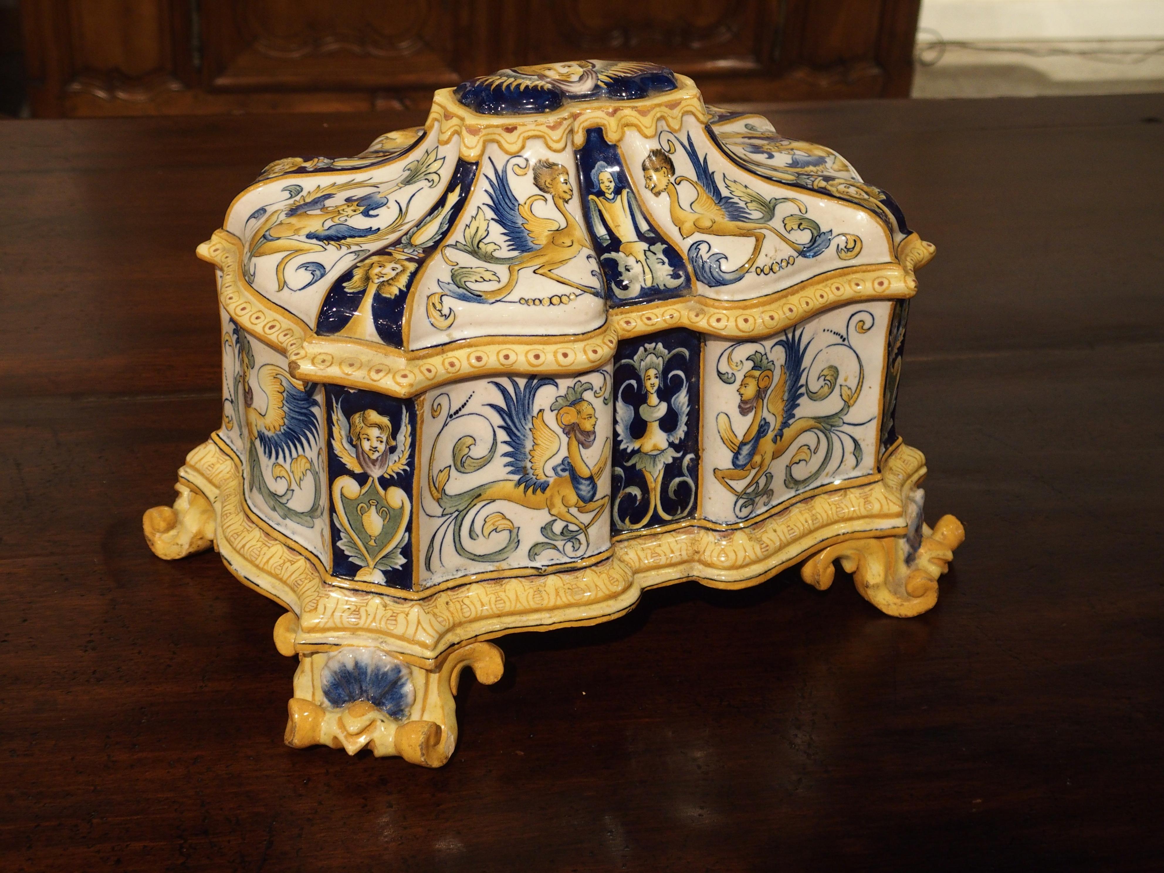 From 19th century, Italy, this shaped majolica box has hand-painted, female, winged, half-figure motifs with varying ornamentation below the waist. The lid has a raised, shaped top with an area at the center which matches the shape of the body.