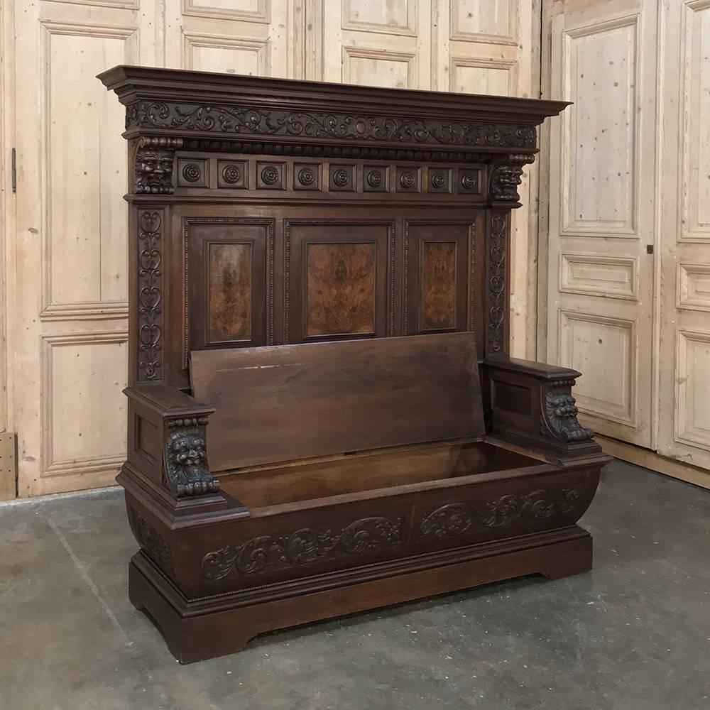 19th century Italian Renaissance walnut hall bench features an abundance of hand-carved sculpture from the full width crown to the base below. Laughing lions appear on the armrest supports. The coffer shaped lower seat portion adds a visual aspect
