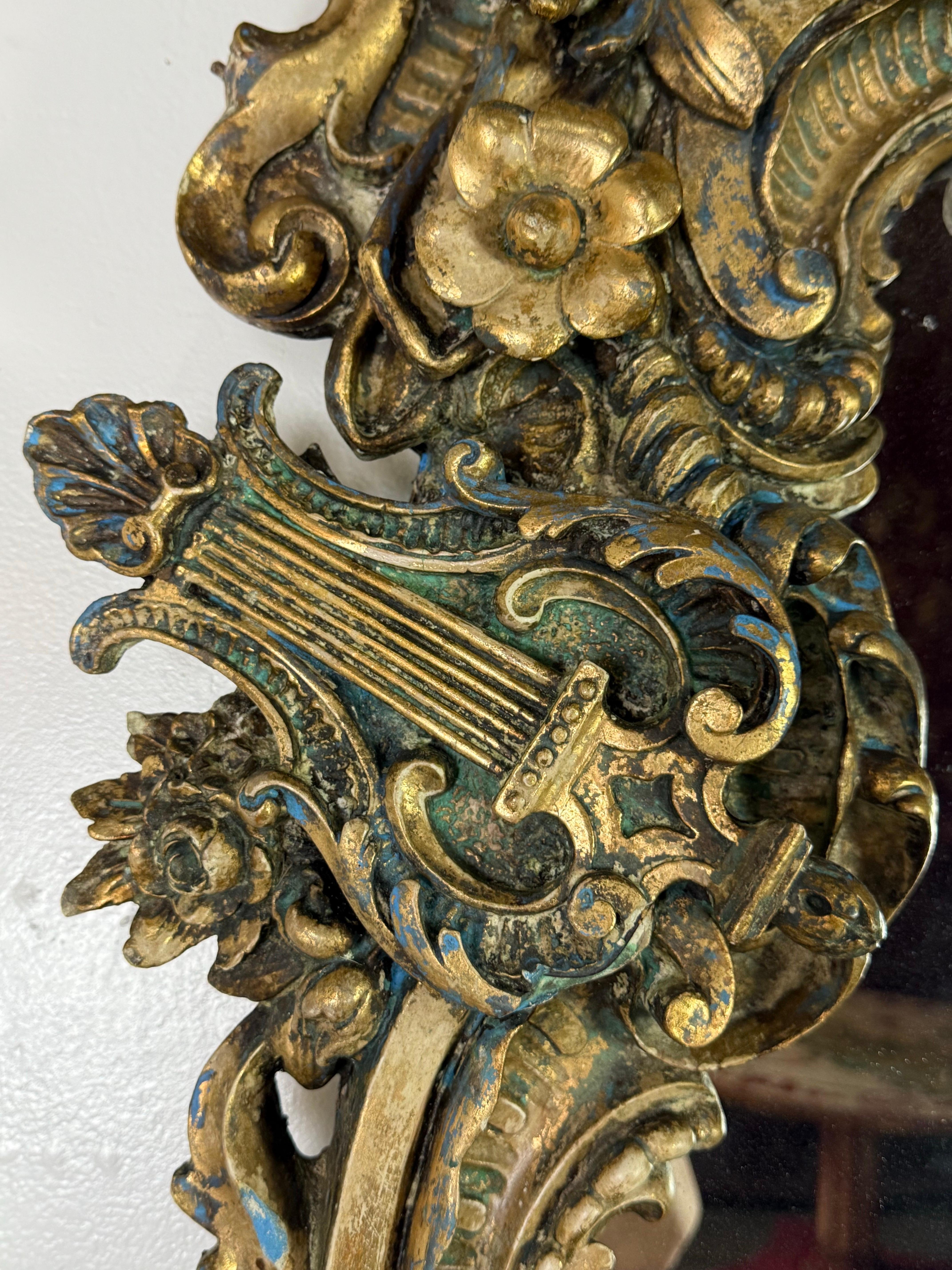 Uno straordinario specchio rococò italiano del XIX secolo in legno dorato riccamente intagliato con dettagli esuberanti e ornamenti figurali. Lo stemma è sormontato da un putto reclinato che legge da un libro aperto, incorniciato da foglie d'acanto