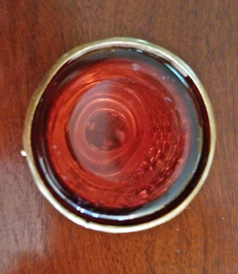Hübsches kleines Ringglas oder Pillendose aus dem 19. Jahrhundert aus dickem weinrotem Glas.
Oben ist eine Miniatur einer Basilika abgebildet, an den Seiten sind vergoldete Metallbeschläge mit schönem Filigran angebracht.
Es handelt sich