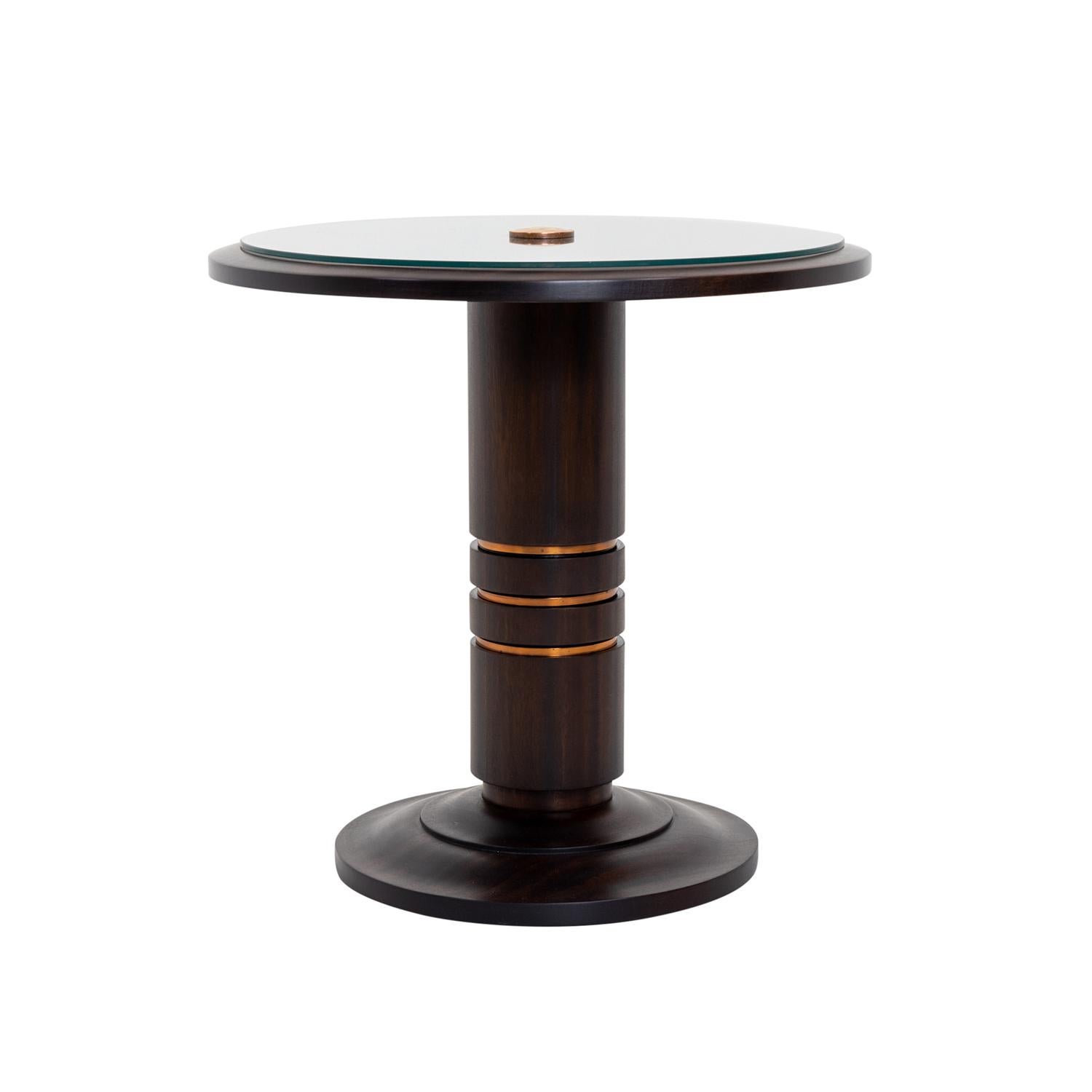 A round, vintage French Art Deco side, center table made of hand crafted shellac polished, partly veneered Honduran Mahogany in good condition. The detailed end table is composed with its original clear glass top which is halted by the slightly