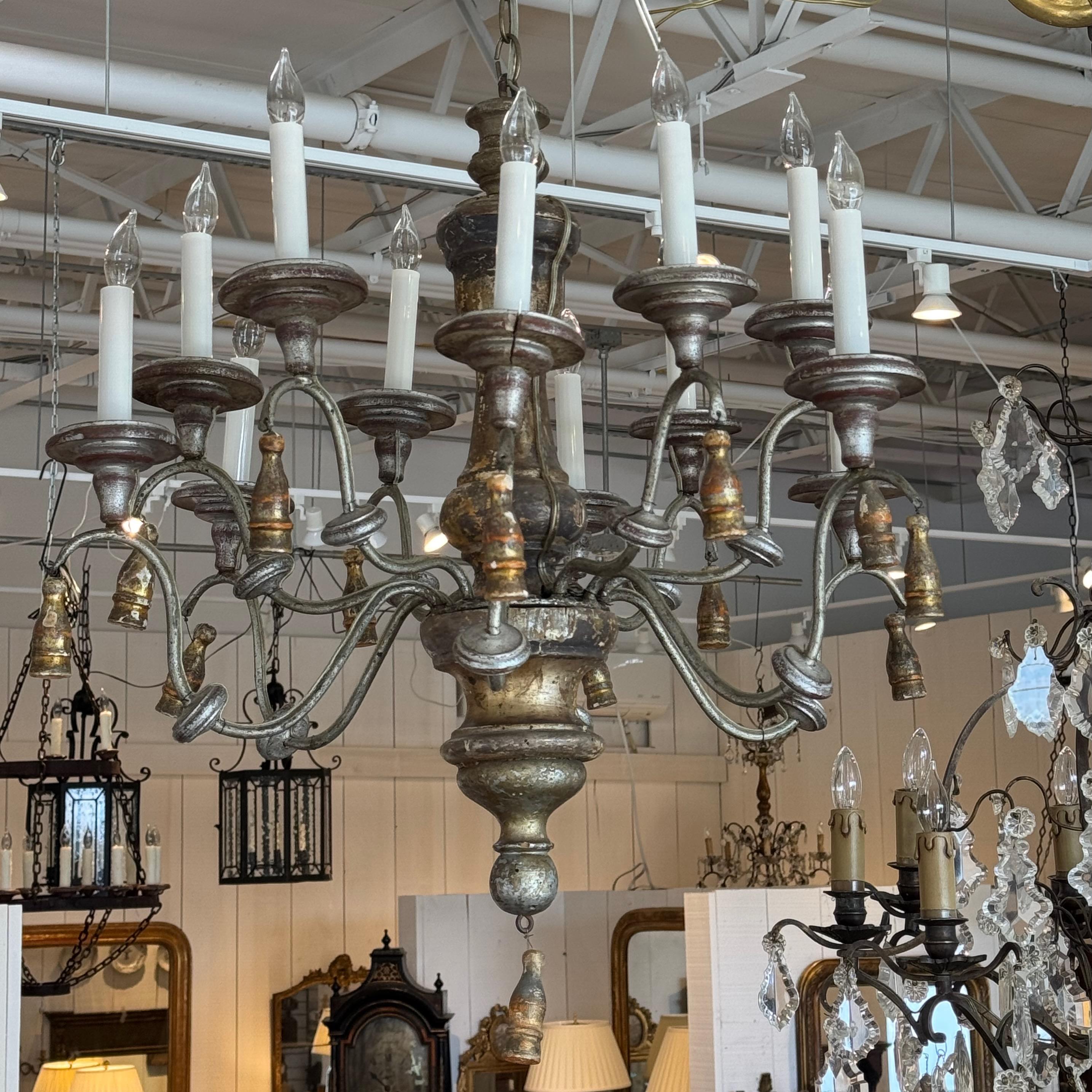 Questo lampadario italiano in argento dorato è caratterizzato da una finitura elegante e consumata dal tempo, con una sorprendente miscela di toni argentati e dorati. La colonna centrale intagliata presenta una patina graziosamente invecchiata,