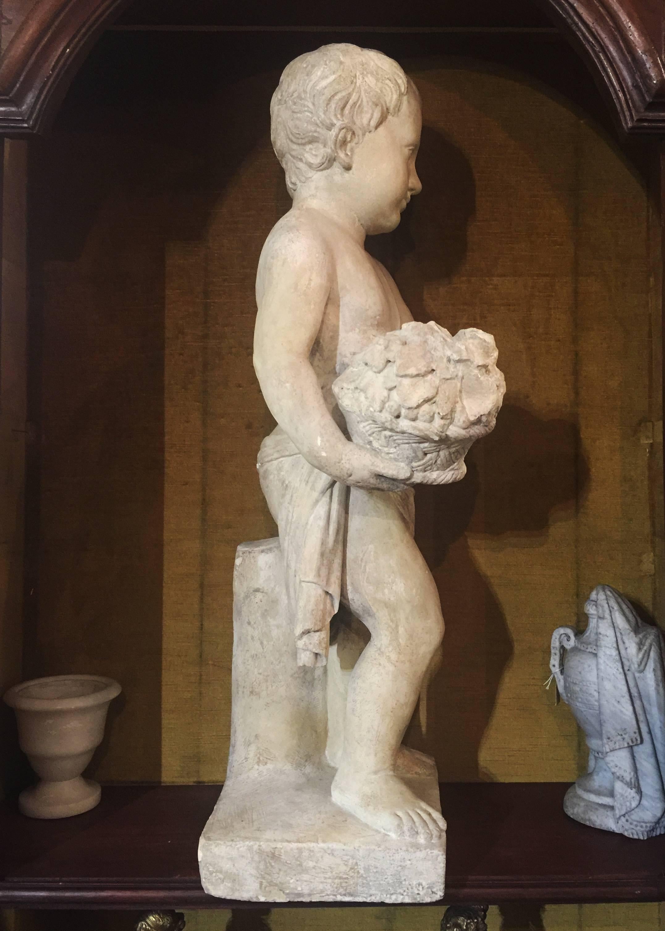 A charming stone statue depicting a small putto holding a basket with flowers.
Italian manufactory from the early 19th century
The sculpture has been cleaned and presents a protective patina.
It could be used as outdoor decoration in the garden
