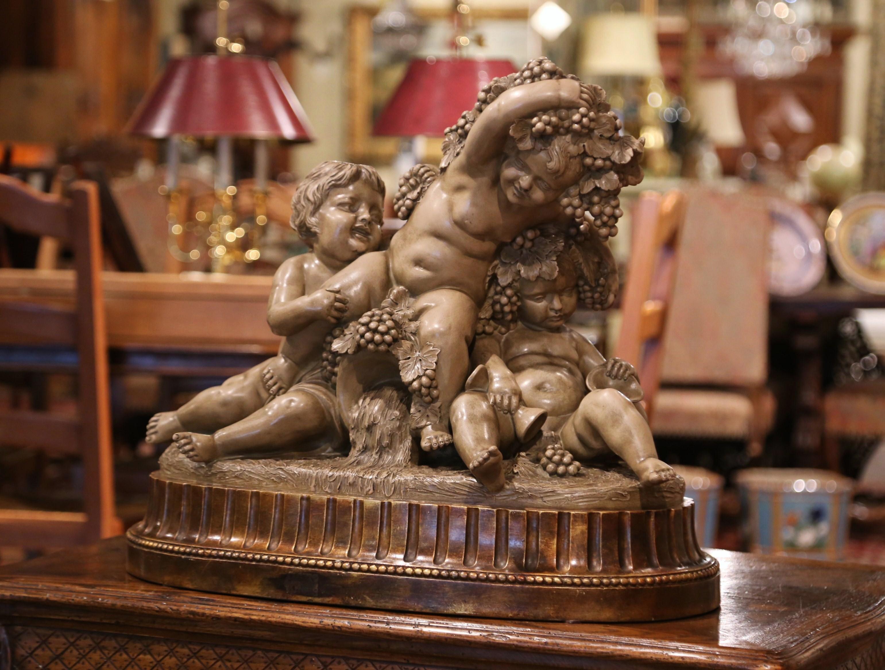This large antique clay cherub composition was crafted in Italy, circa 1890. Standing on an oval base, the carved sculpture depicts three sited playful Bacchus children all covered with grape and vine decor; the cherubs are nicely carved with