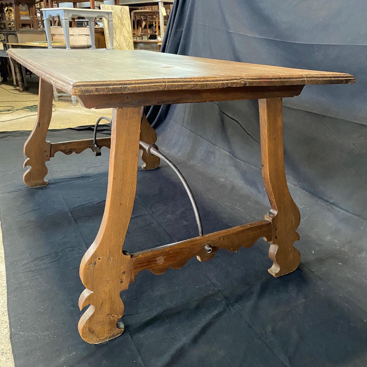 Beautiful early 19th century Italian baroque dining table in walnut with rustic plank top resting on carved H form trestle legs and hand forged iron stretchers. A great table as a console under a large contemporary painting, in a wine cellar, or as