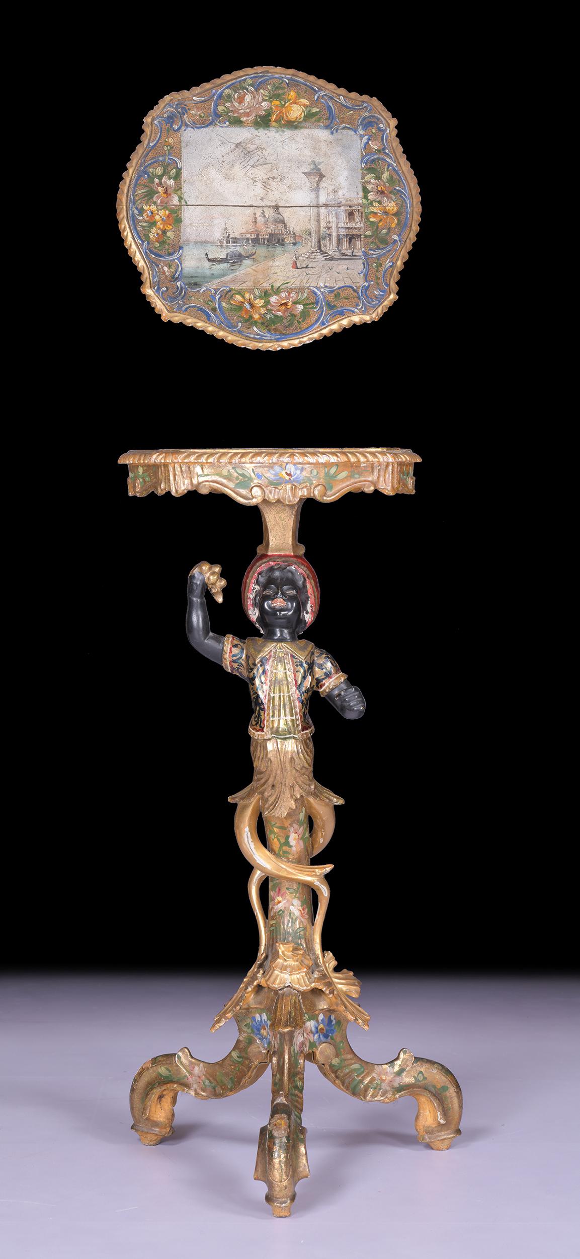 A good 19th century Venetian Italian Gondolier torchere stand, of typical Venetian form, polychrome painted with the softwood carved figure holding the shaped silvered top and a bunch of grapes raised upon a Rococo style triform base, with a painted