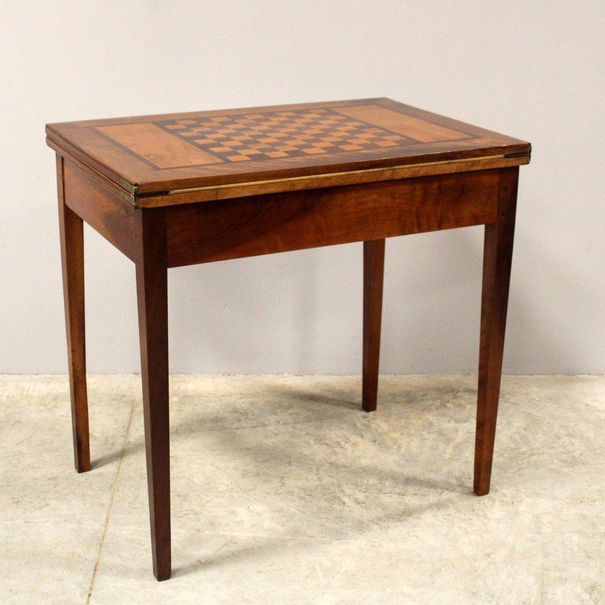 An Italian walnut and mahogany game table from the 19th century with checkerboard marquetry sliding top and tapering legs. Behold a statement of Italian craftsmanship—this 19th-century Italian walnut and mahogany game table captivates with its