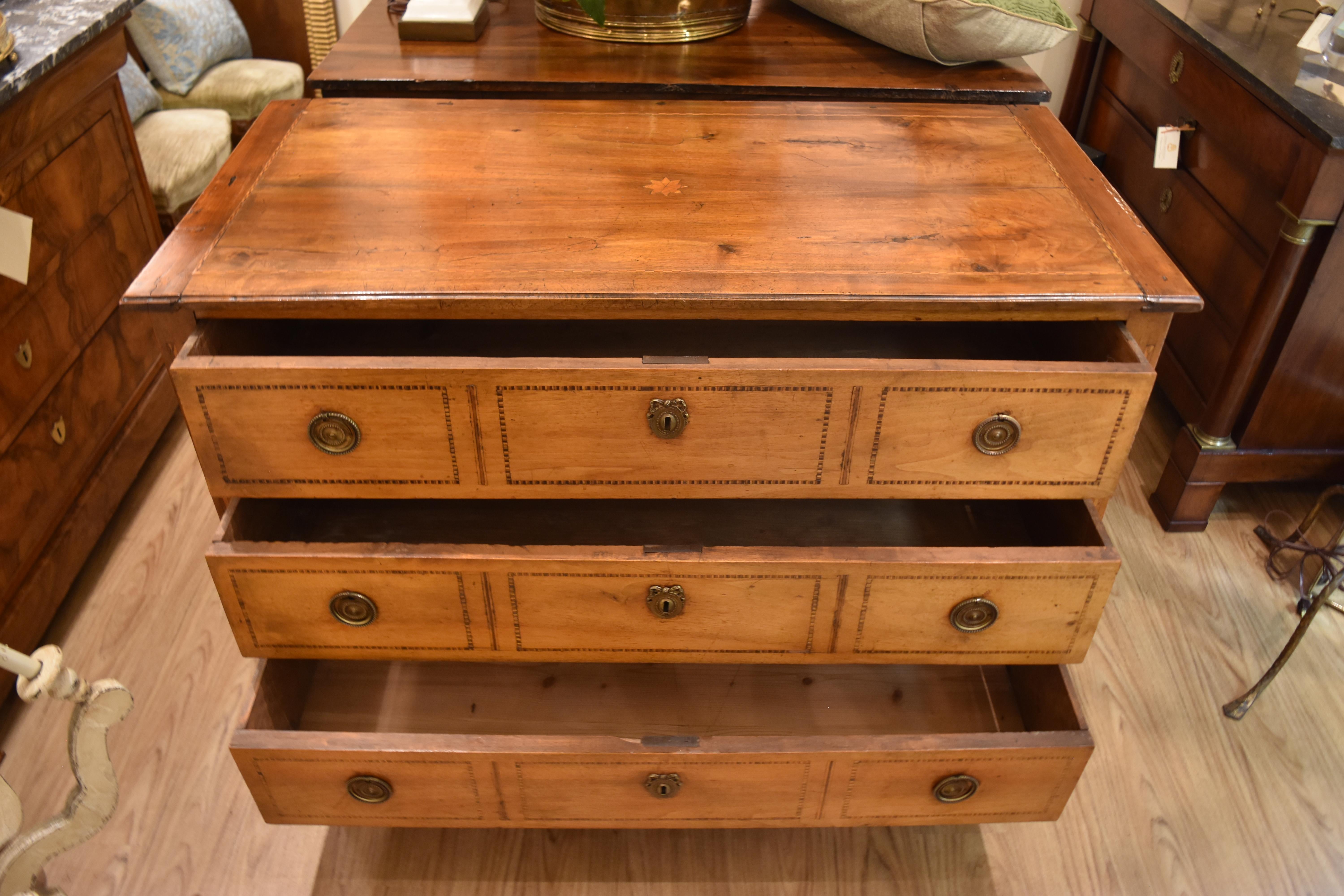 This 19th century Italian walnut commode features three working drawers all with the original pulls and key escutcheons. The top has an inlayed star design and the top perimeter and drawer fronts all feature an inlayed geometric design. The front