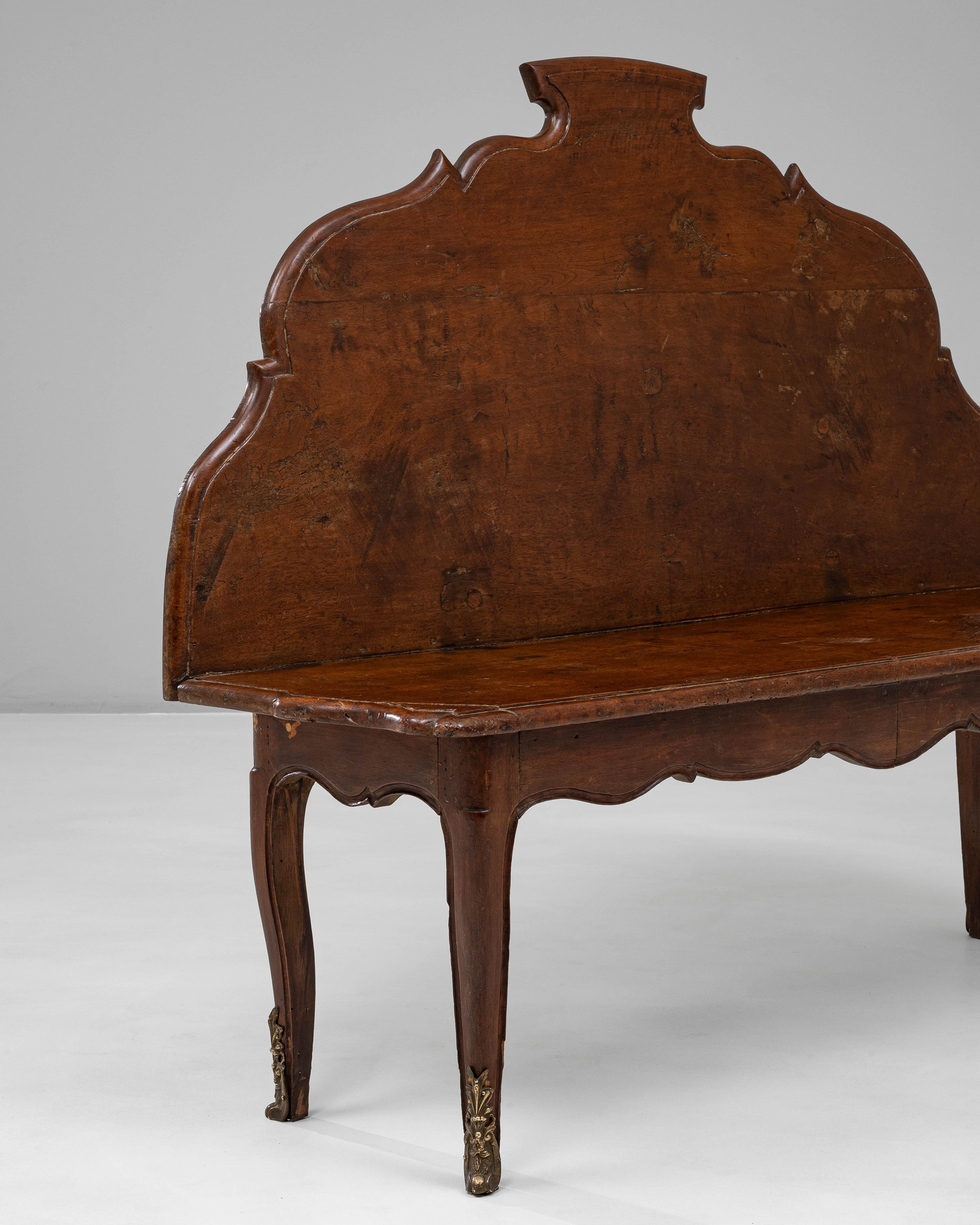 Este banco de madera italiano del siglo XIX presenta un llamativo respaldo escultórico que define su elegante y expresiva silueta. Fabricado en madera de tonos intensos con una pátina cálida y envejecida, el banco presenta una cresta amplia y