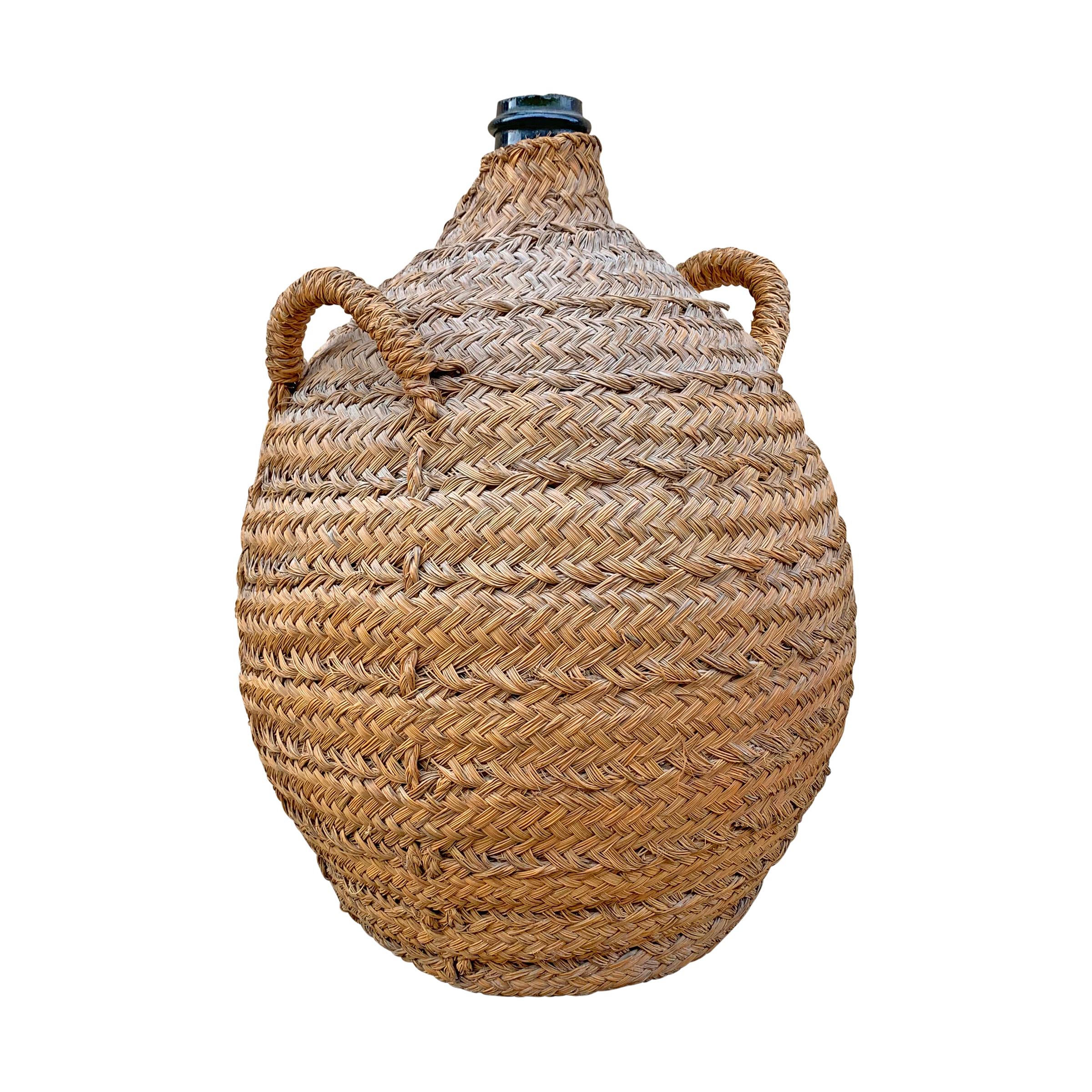 A handsome 19th century Italian hand blown green glass wine jar covered in a handwoven wicker basket to protect from bumps and bruises.
