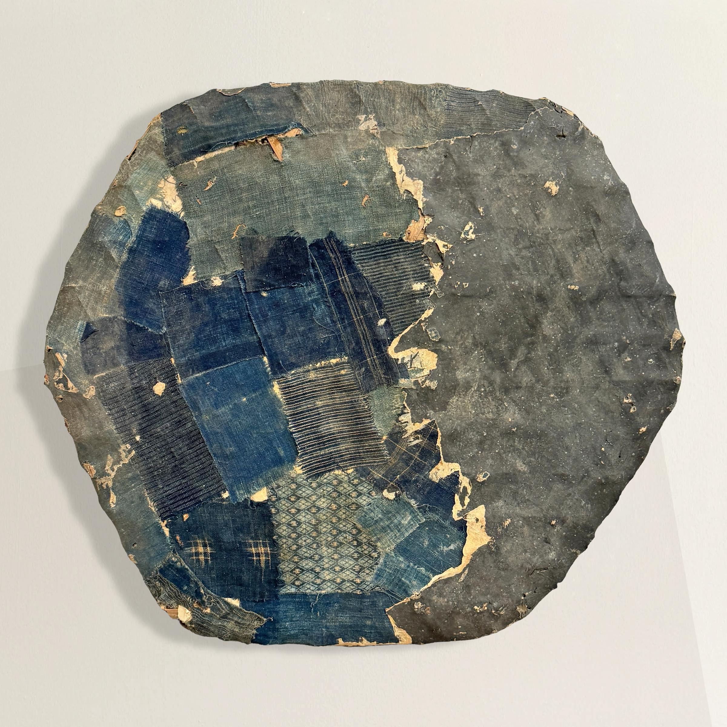 This 19th-century Japanese woven bamboo basket, likely used for grain or rice, transcends its industrial origins to become a stunning contemporary artwork. Covered in a mosaic of indigo cotton Boro textile fragments, the basket showcases the