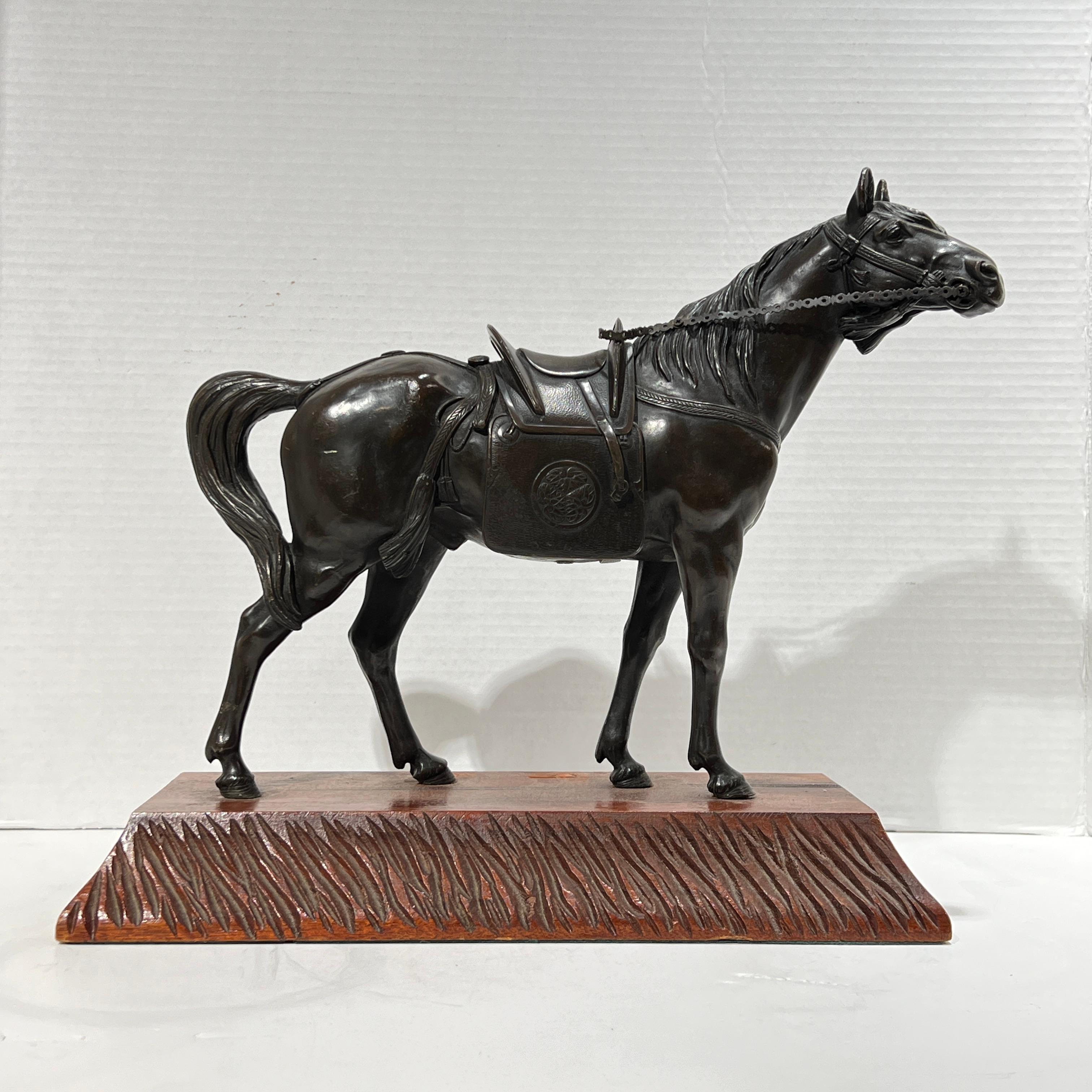 Antique (19th century) patinated bronze figurine of a horse with bridle and saddle, mounted on later wooden pedestal.  Figurine alone measures 14 by 11 by 3.5 inches.  Total height with base 13 inches and depth of the base is 6.5 inches.  Saddle