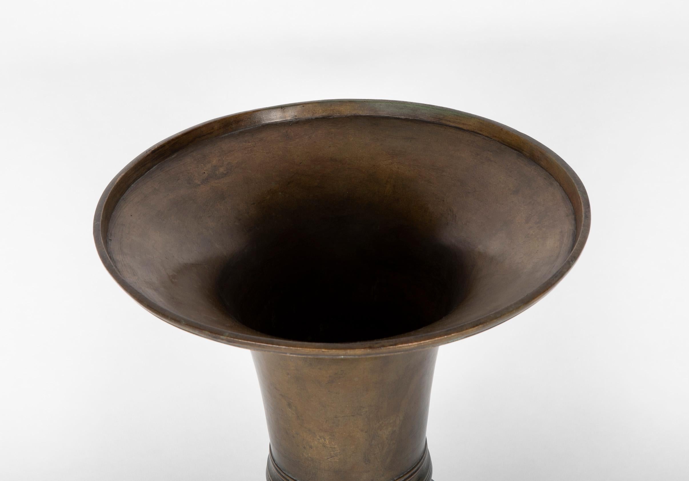 A large scale 19th century Japanese bronze vase of trumpet form with a wide mouth over a narrow waist supported by a stepped base. The form shows the influence of Chinese Archaic bronzes. A great setting for long stem flowers or bouquets. This