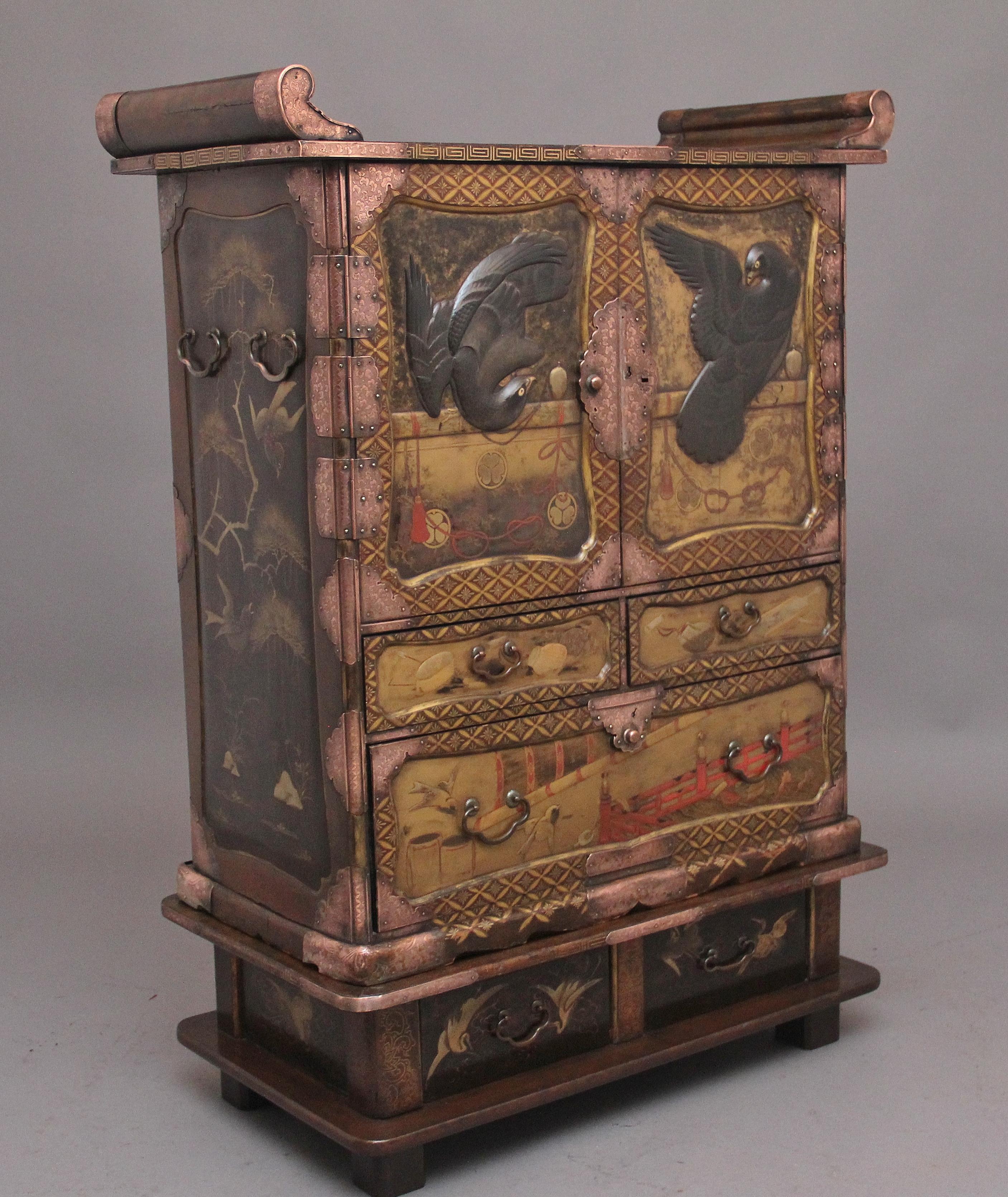 A highly decorative 19th Century Japanese gilt lacquered cabinet from the Meiji period (1868-1912) the double hinged doors decorated with two eagles in relief, each standing on a pole in a shaped panel, opening to reveal two shelves and five