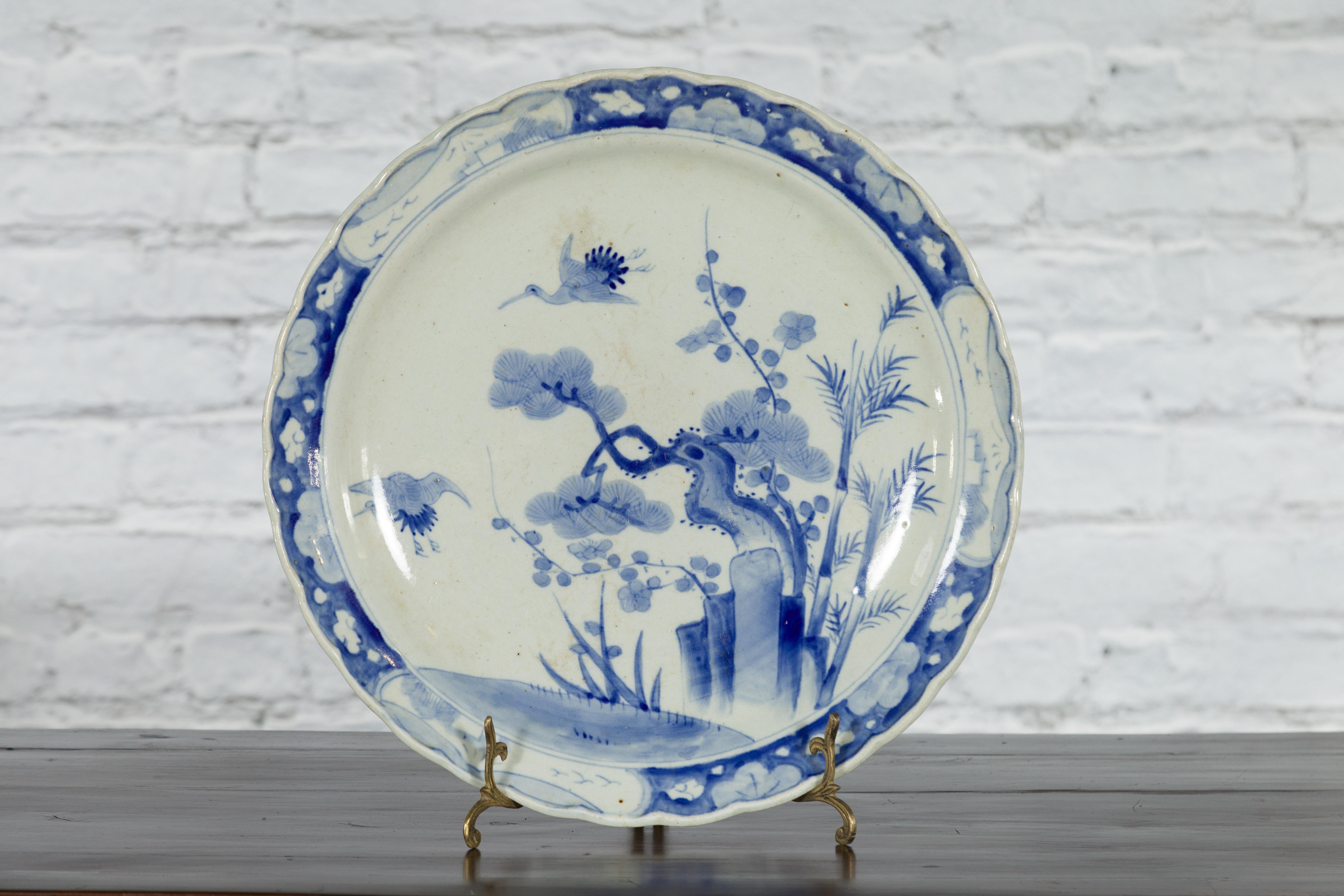 A Japanese porcelain charger plate from the 19th century, with hand-painted blue and white blooming tree, rocky formation and bird décor. Created in Japan during the 19th century, this porcelain plate features a delicate blue and white décor