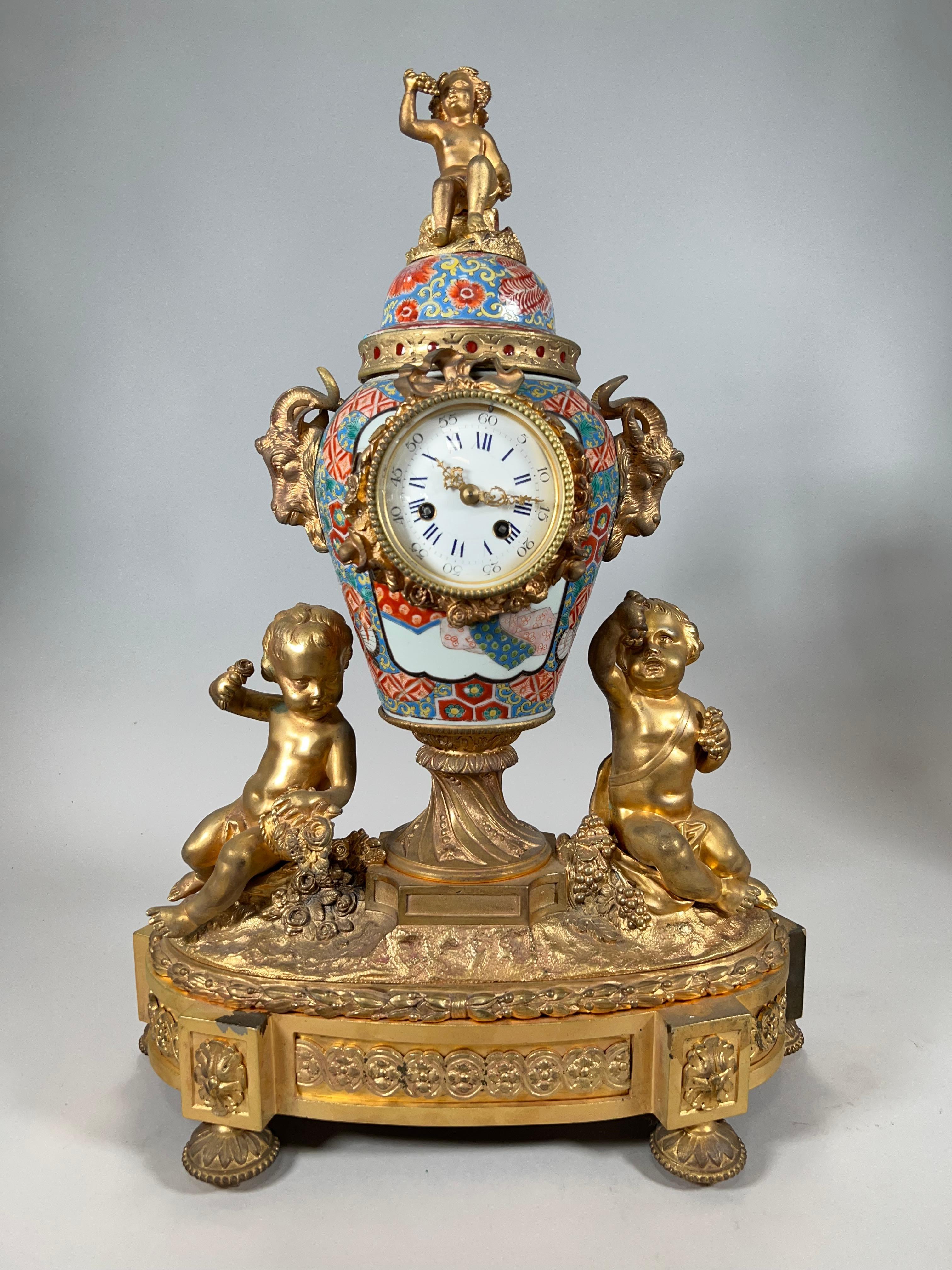 JAPANESE IMARI PORCELAIN AND ORMOLU MOUNTED MANTEL CLOCK, 19TH CENTURY urn shaped with three ormolu mounted cherubs with Roman Numeral and Arabic dial. Dimensions Height: 22