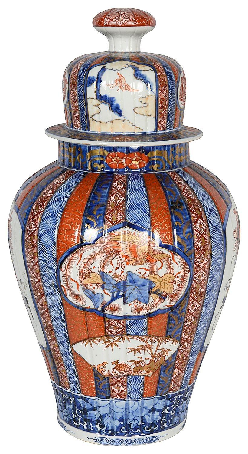 A very good quality late 19th Century Japanese lidded Imari vase, having wonderful bold colouring to the classical motif decoration, set in scolloped vertical bands with inset hand painted panels depicting exotic flowers on a table, mythical dragons