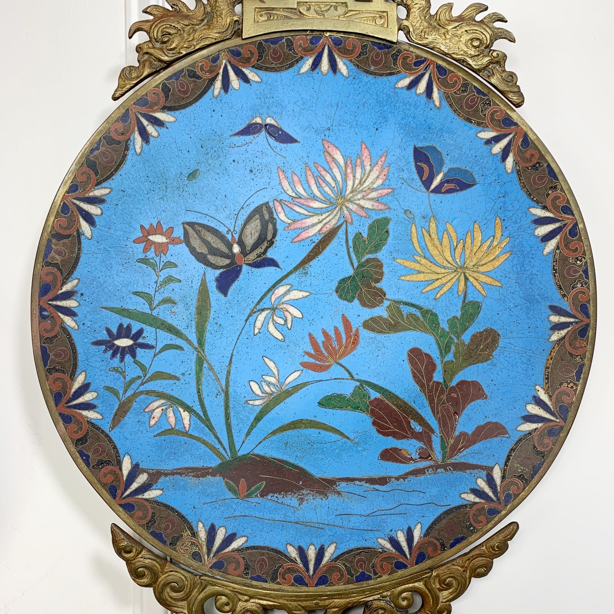 A beautiful pair of Japanese Meiji period enamelled plates, cloisonne decorated in bright turquoise with butterfly and flowers, in reds, greens, pinks and ochre. Plates date to the 19th century and have been later mounted in brass temple dragon