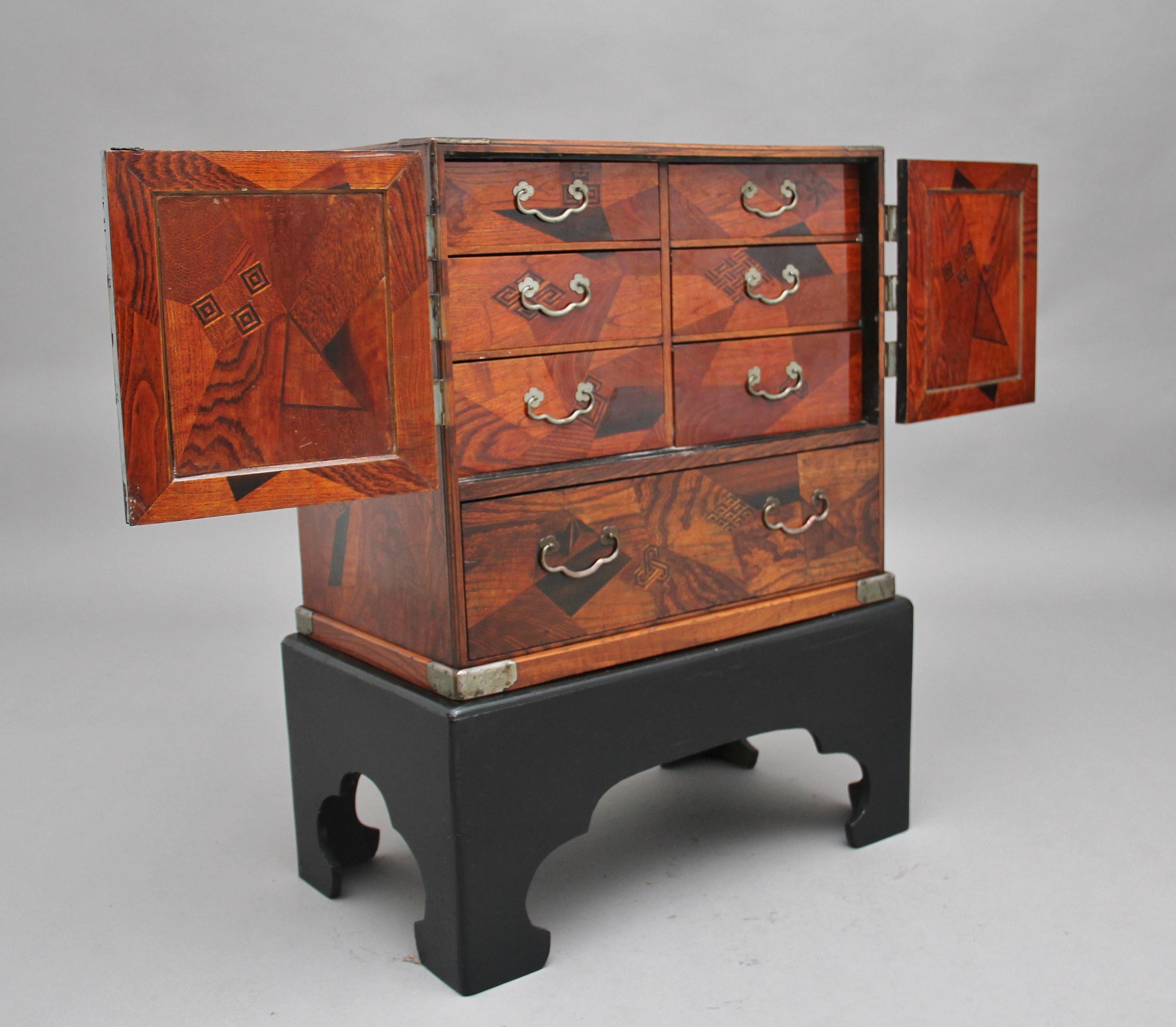 19th century Japanese parquetry kodansu from the Meiji period, the rectangular cabinet with a pair of paneled doors painted with cockerels amidst flowering branches, applied with ornate brass spandrels and hinges, enclosing six conforming parquetry