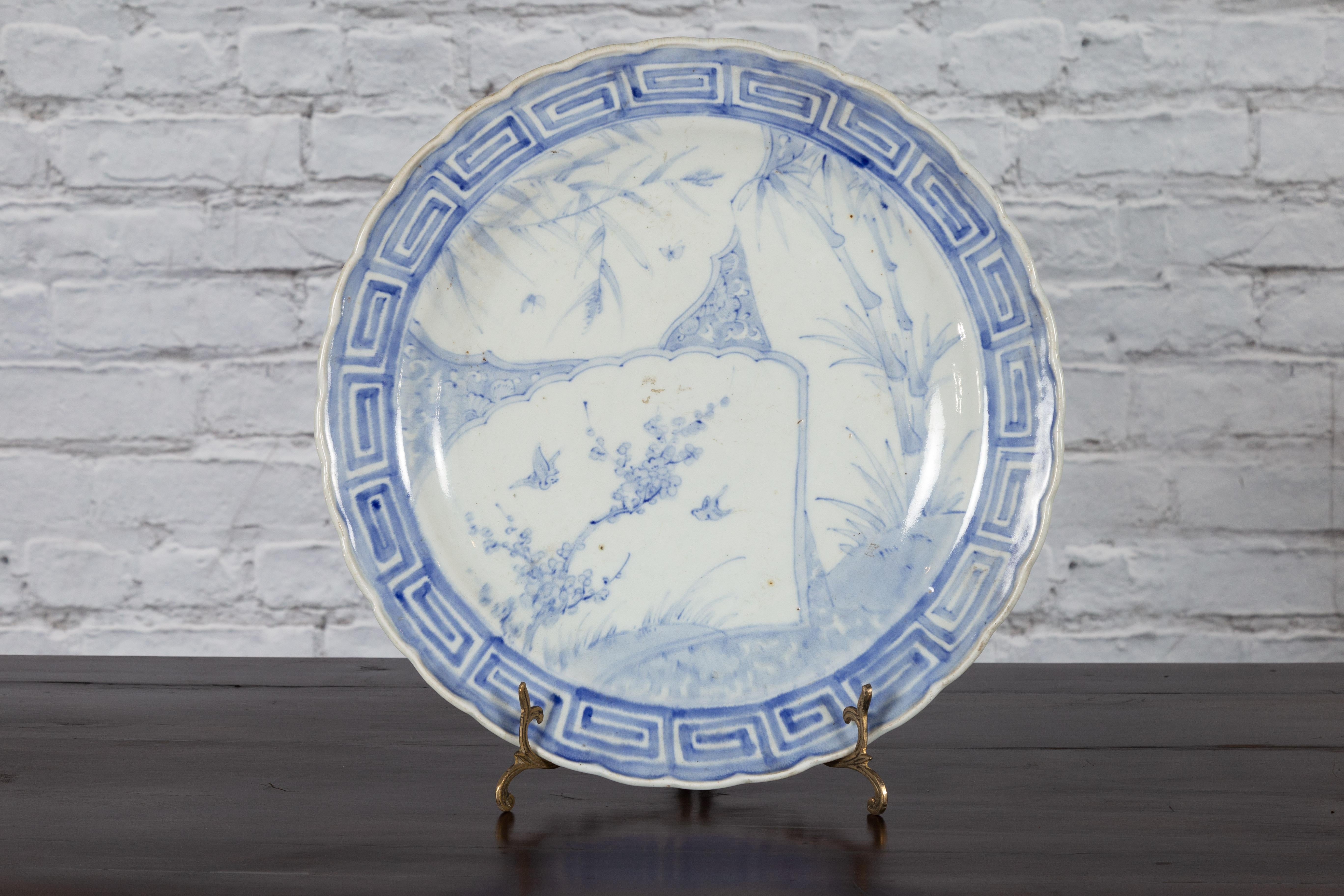 A Japanese hand-painted porcelain plate from the 19th century, with blue and white birds, foliage and bamboo décor. Created in Japan during the 19th century, this porcelain plate features a delicate blue and white décor depicting birds flying around