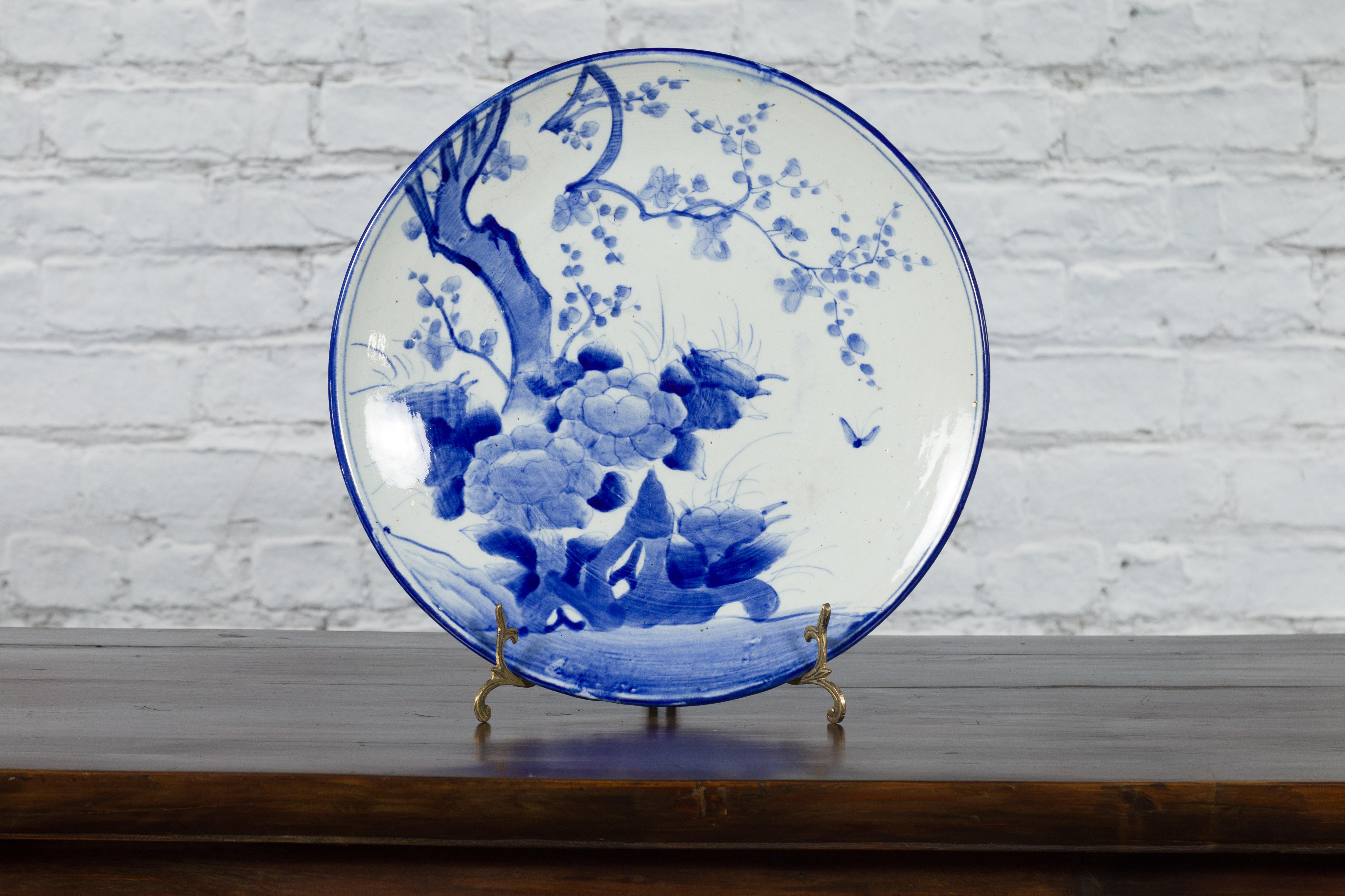 A Japanese hand-painted porcelain plate from the 19th century, with blue and white tree, foliage and butterfly décor. Created in Japan during the 19th century, this porcelain plate features a delicate blue and white décor depicting a blooming tree