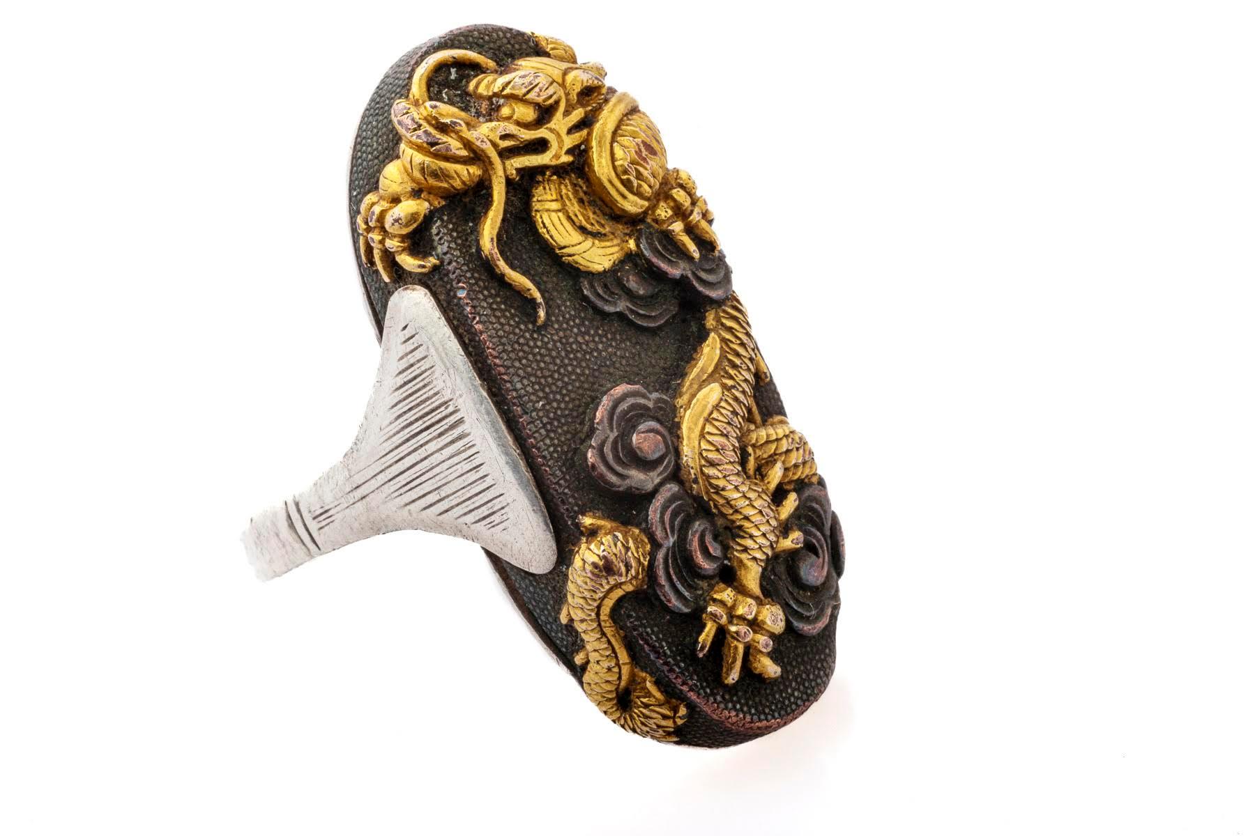 A Japanese Shakudo ring with a lavish show of gold on a textued charcoal gray background. It has excellent finger coverage at 1 5/8 inches high. The gold dragon is striking as it wriggles, showing its claws,  from bottom to top of the ring. There is