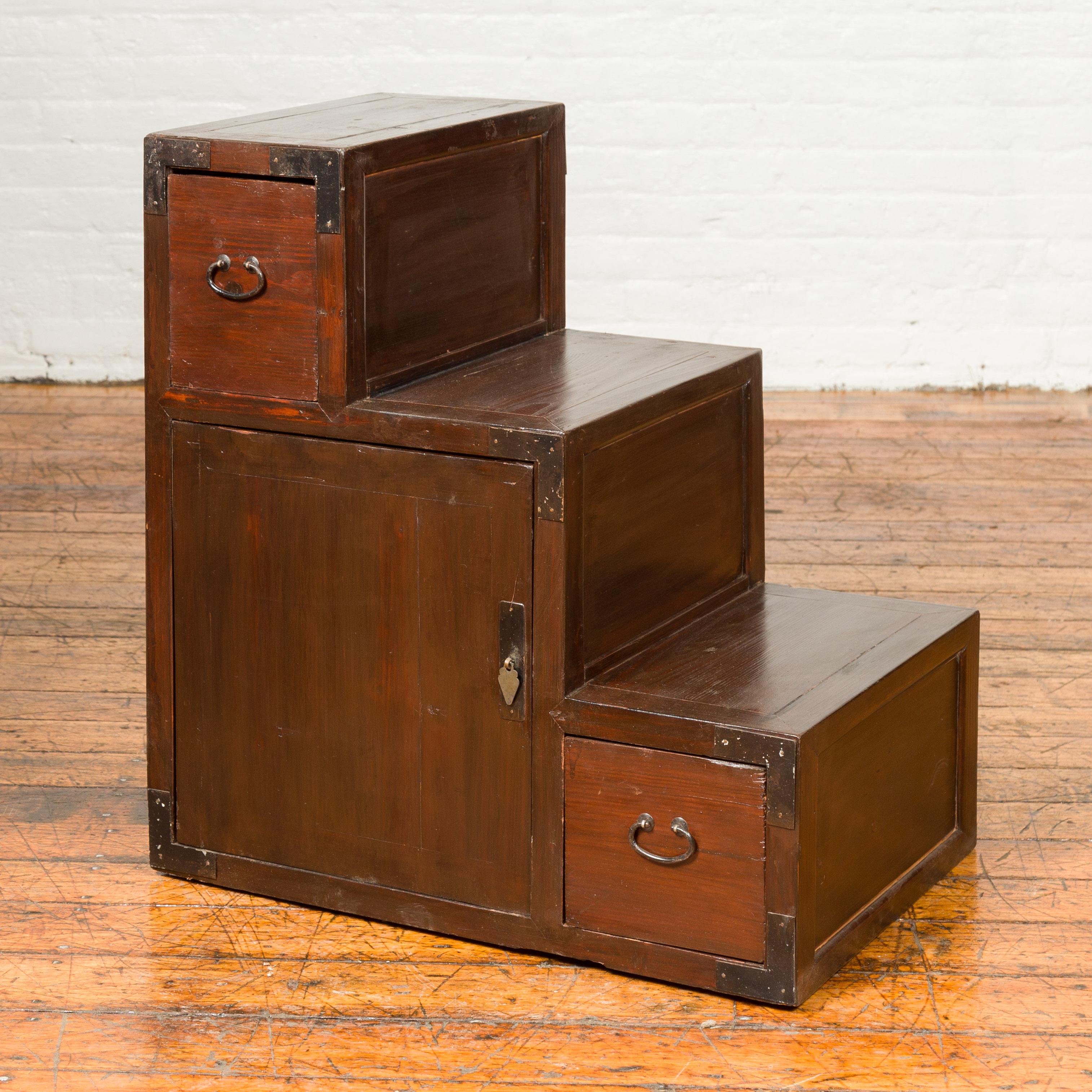 A Japanese staircase tansu cabinet from the 19th century, with two drawers and doors. Born in Japan during the 19th century, this staircase tansu features a convenient stepped storage unit presenting a warm patina. Ideal to display decorative items
