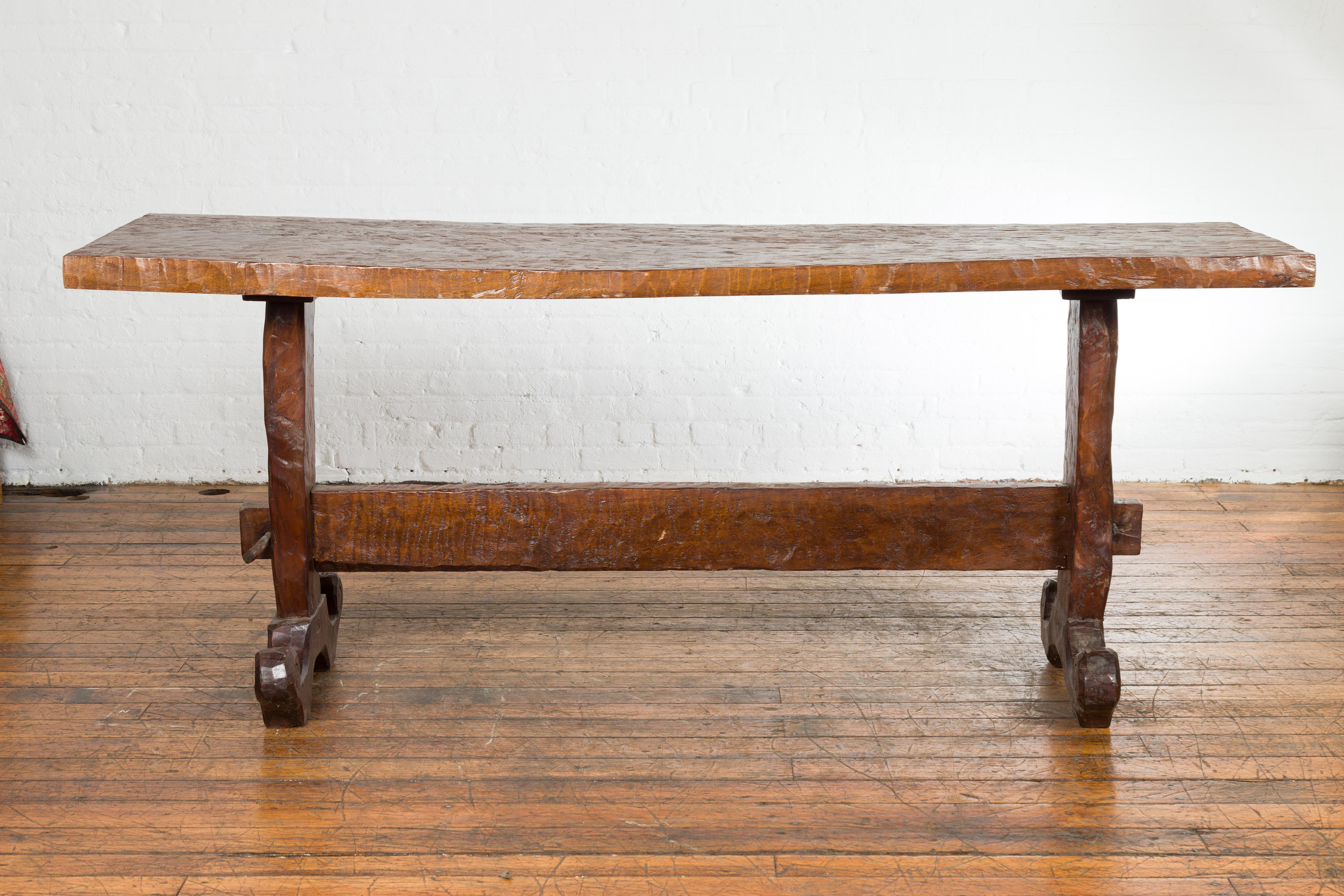 An antique Javanese rustic console table from the 19th century with uneven rectangular top and trestle base. Indulge in the charm of rustic Indonesian design with this 19th-century Javanese console table. This antique piece showcases a trestle base,