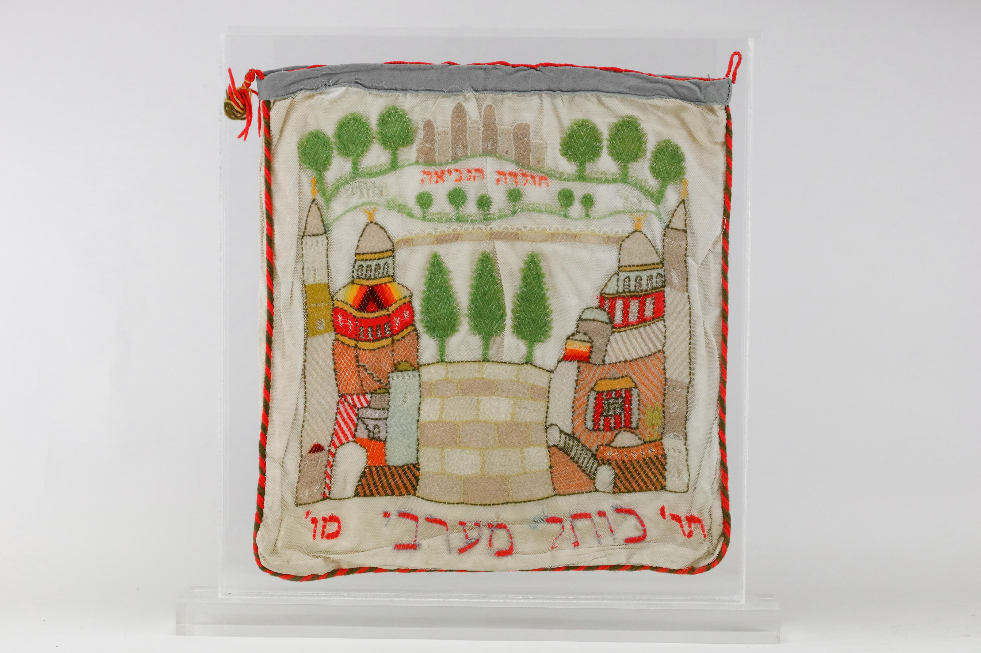 An Intricate Jerusalem Textile, made in Jerusalem, 1886.
Double-sided large pouch. Wool thread embroidered on cotton net. One side has a lion and stag holding flags reading “Jerusalem” in Hebrew, which flank a crowned Ten Commandments. Titled in