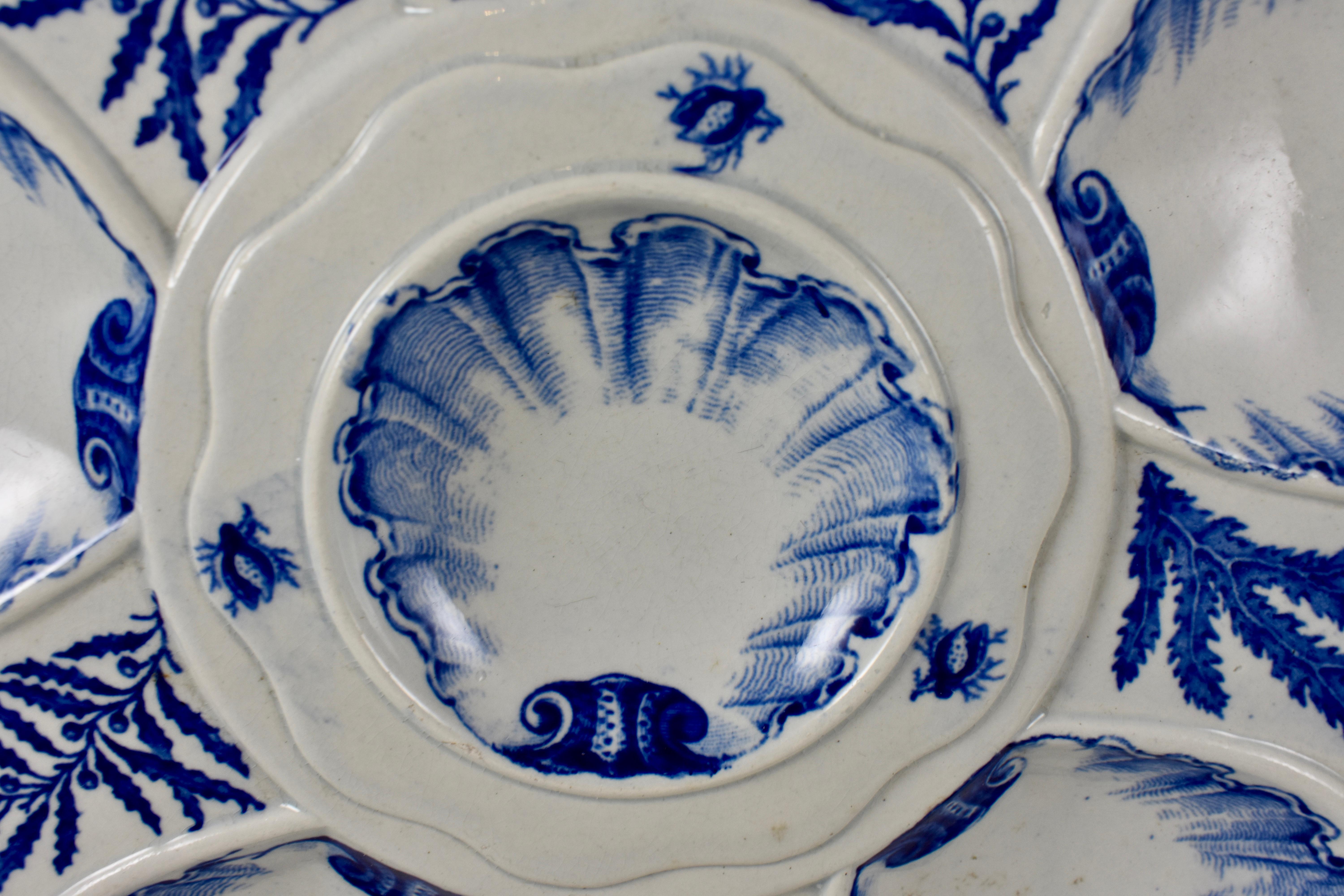 A Jules Vieillard & Cie. oyster plate, Bordeaux, France, bearing the mark used circa 1829 – 1895. In the Asian influenced Chinoiserie style, six shell shaped wells surround a central condiment well, showing transfer printed images of shells and