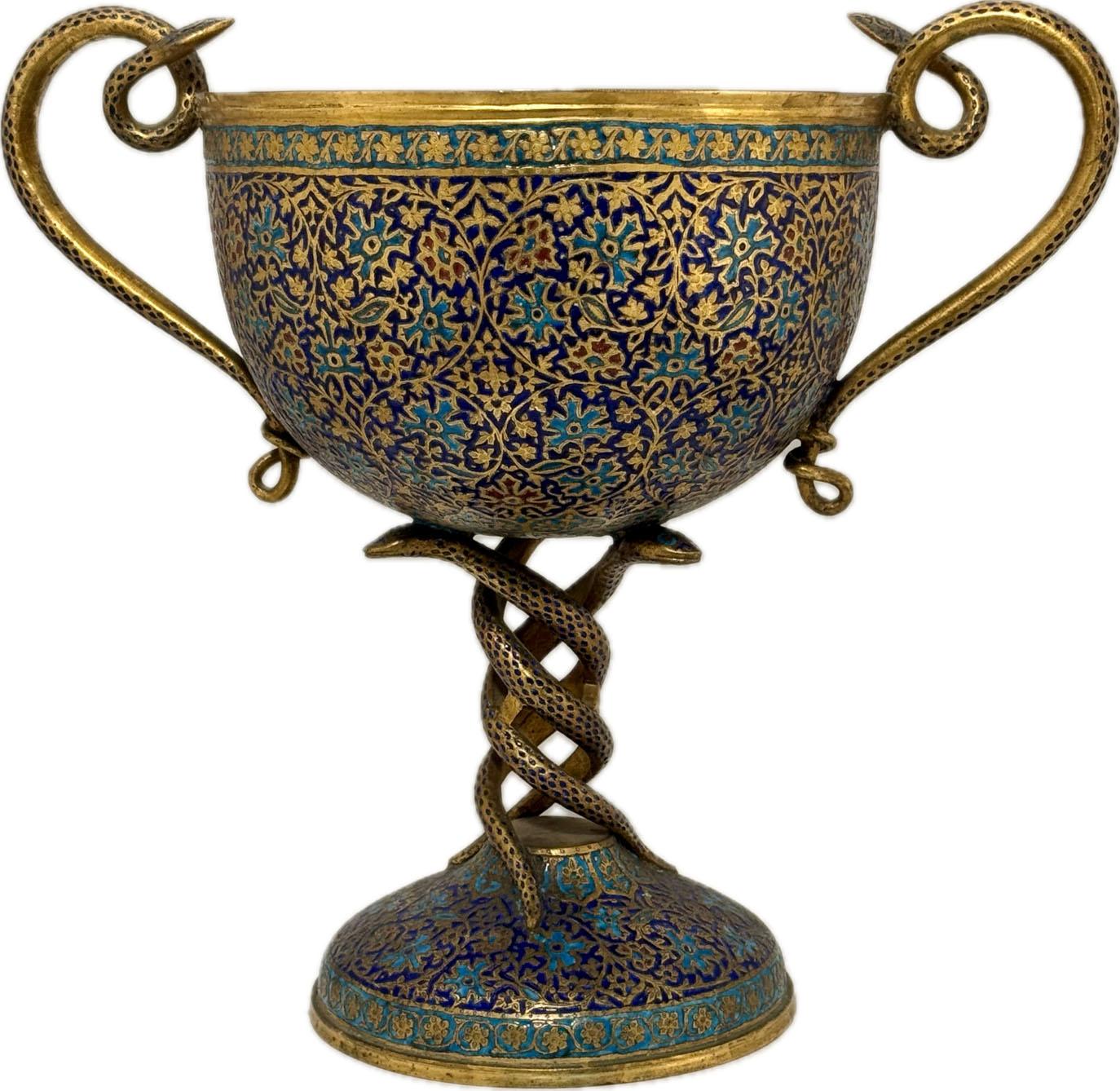 This large and highly decorative cup is supported on a domed base. The stem is formed as two intertwined snakes, which terminate as handles, the snakeheads peeping over the rim. It is elaborately worked with trailing fronds and stylised blue and