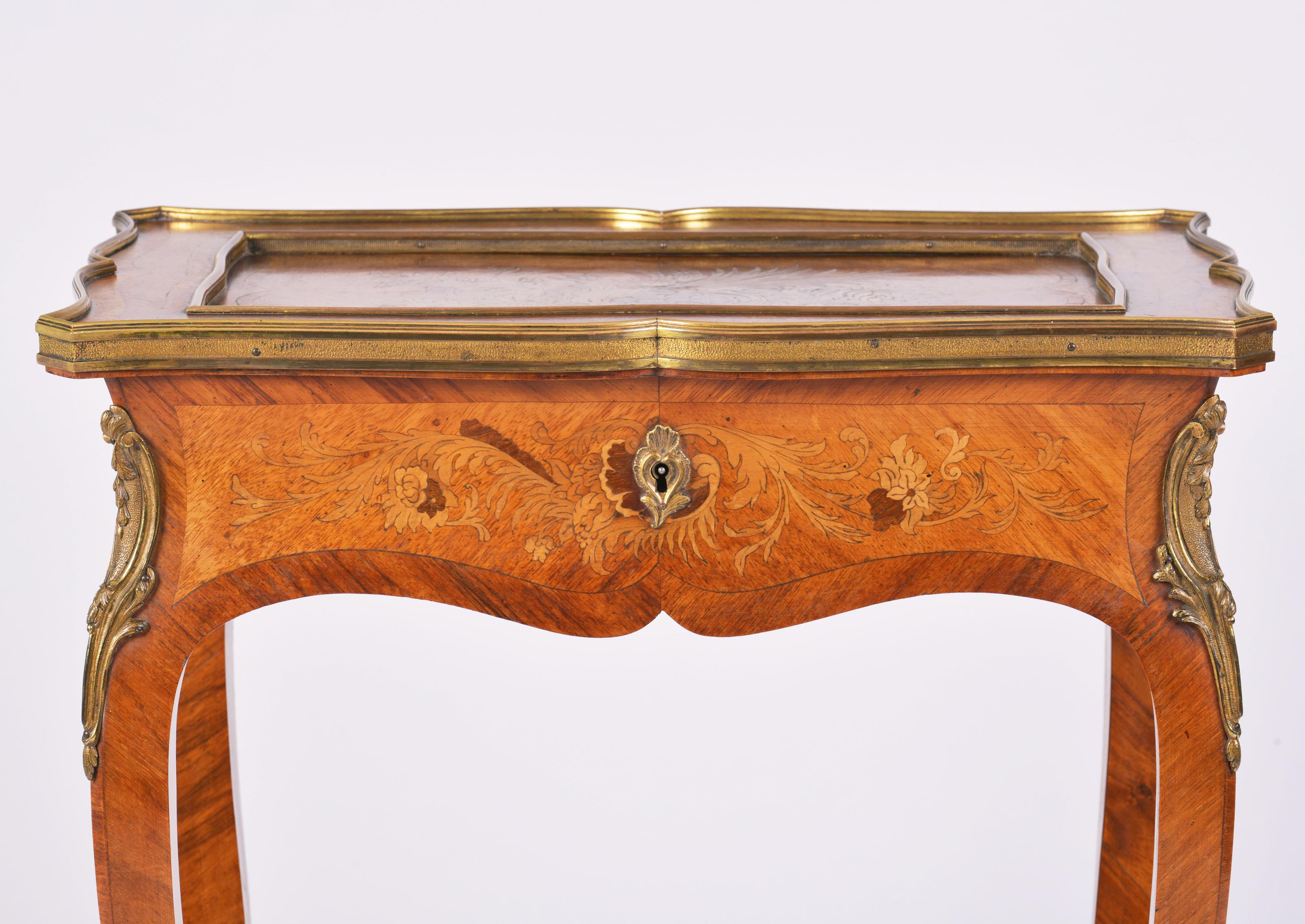 This outstanding and delicately shaped 19th century king wood bijouterie table features intricately designed marquetry inlay work with ornate ormolu mounts and trims. It has a serpentine shaped top with a yellow silk damask lining the inside box and