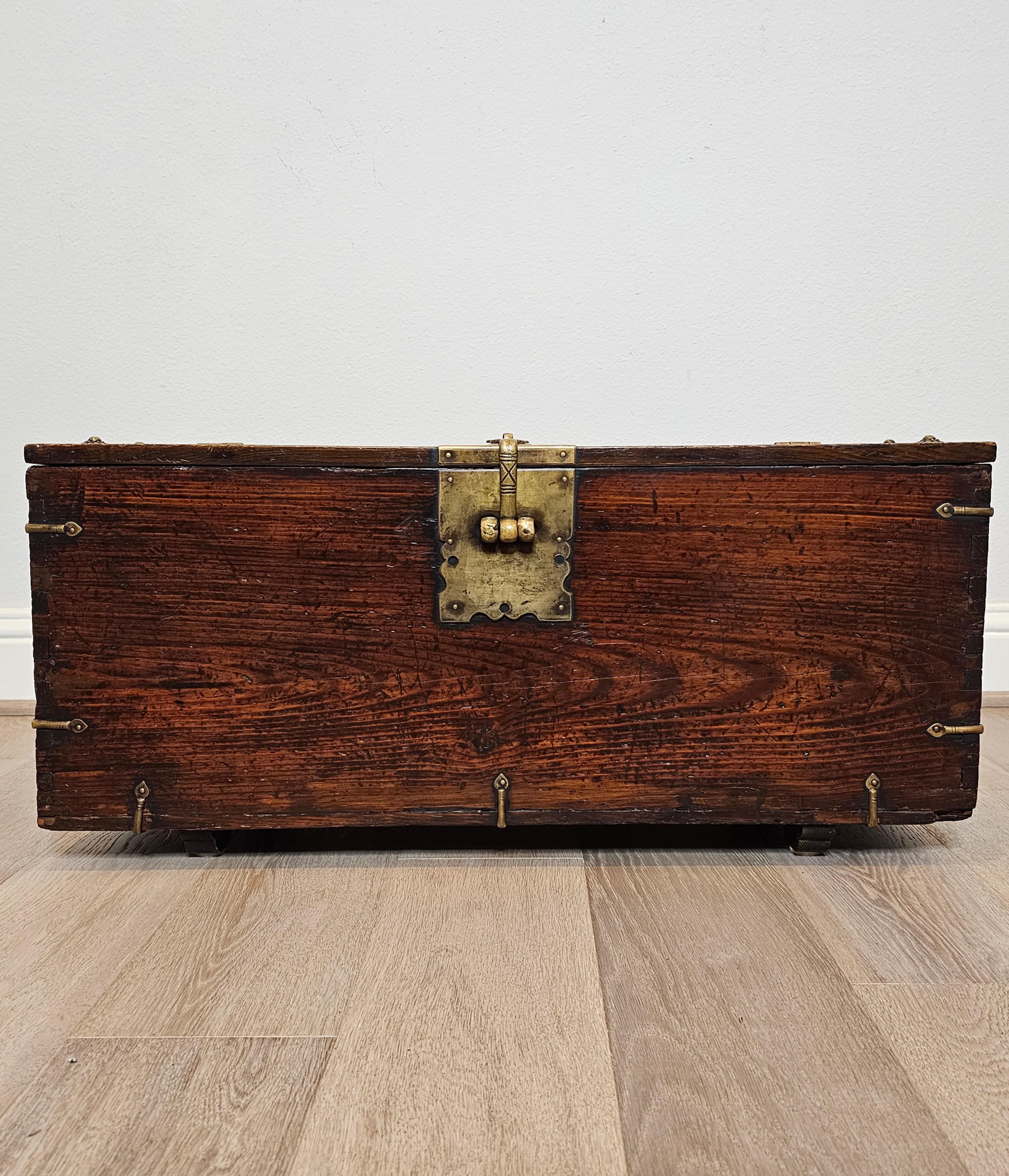 A charming antique Korean wooden money chest with beautifully aged warm rustic distressed patina. Rectangular hardwood case with exposed tongue and groove joinery, heavy brass hardware and decorative patinated brass strap supports, having a partial