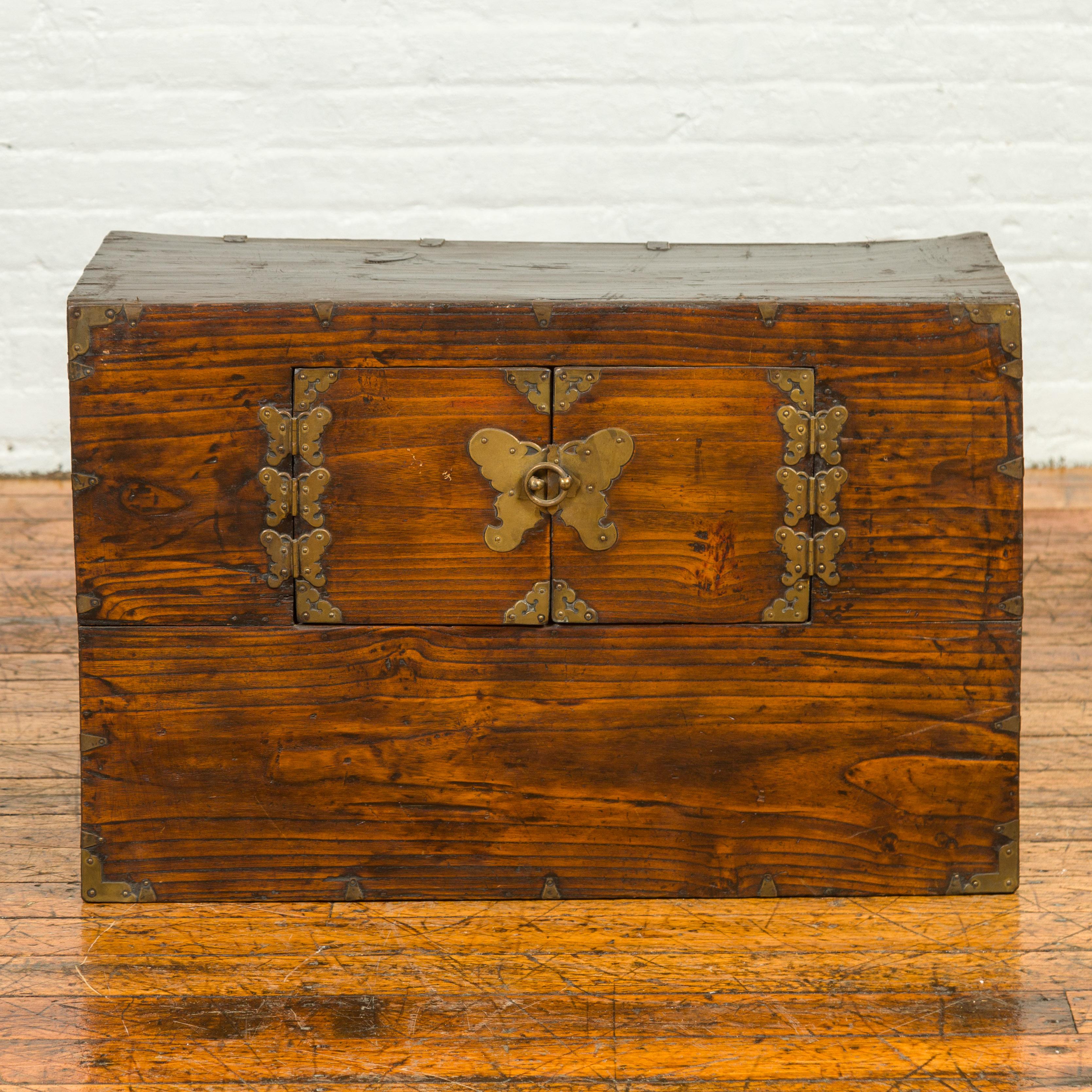 A Korean wooden side chest from the 19th century with double doors and brass butterfly-shaped hardware. Crafted in Korea during the 19th century, this small cabinet features a rectangular top sitting above a simple façade showcasing a pair of small