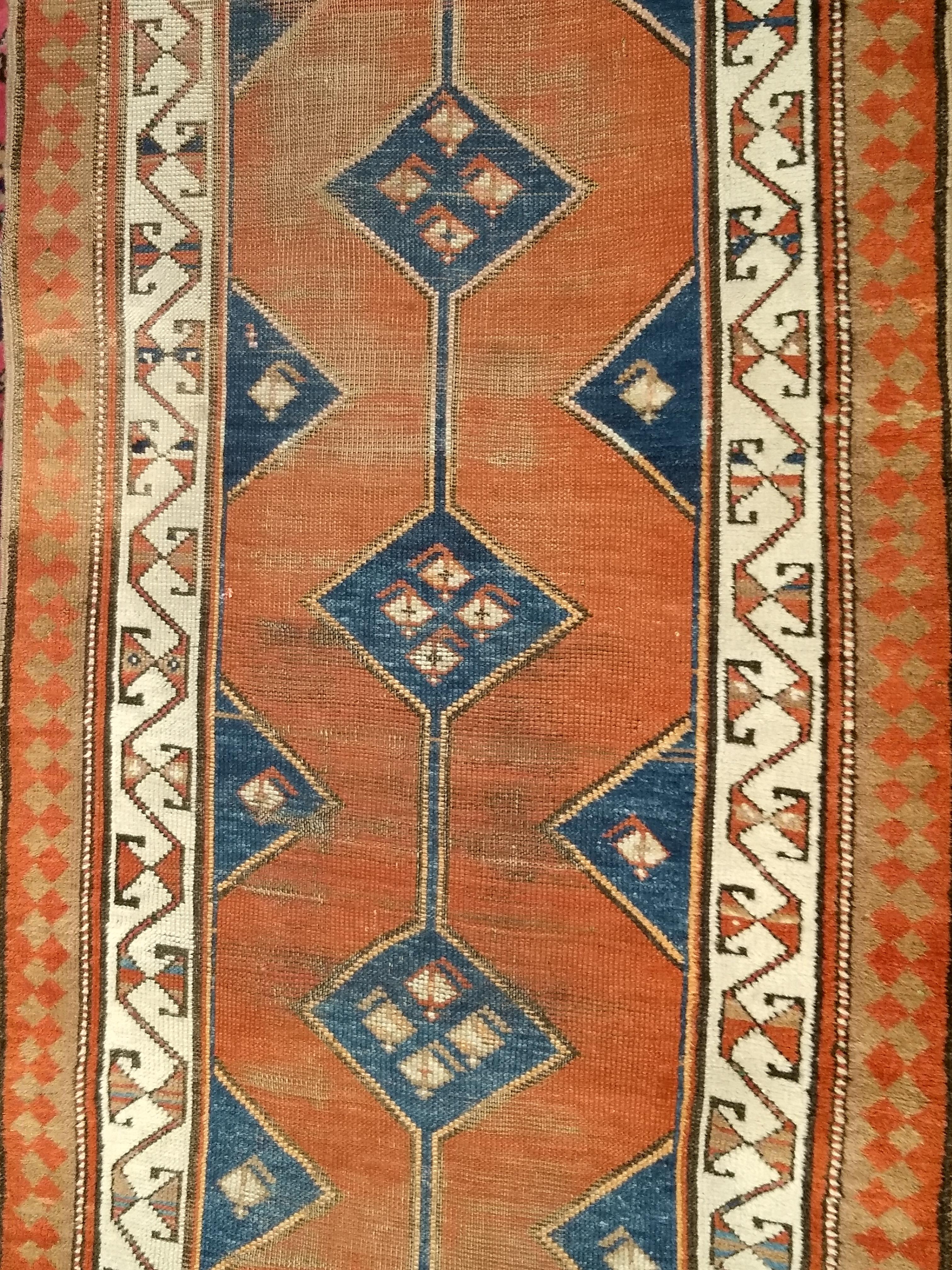 Runner persiano curdo annodato a mano del XIX secolo con motivo geometrico.  Il disegno consiste in otto piccoli medaglioni assiali in blu navy abrasivo su un campo color terracotta.  Il design è molto aperto e ordinato, con piccole forme di paisley